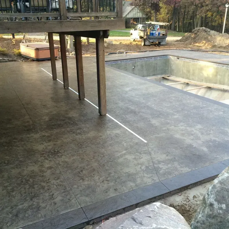 A concrete deck with a swimming pool in the background