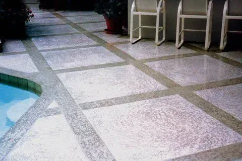 A tiled floor next to a pool with chairs and tables.