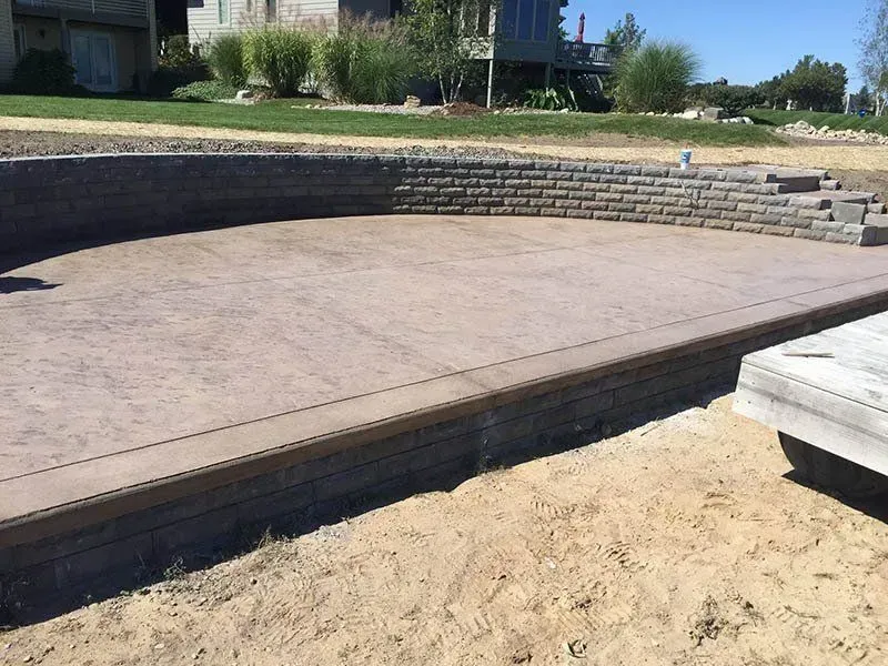A concrete patio with a brick wall and a house in the background