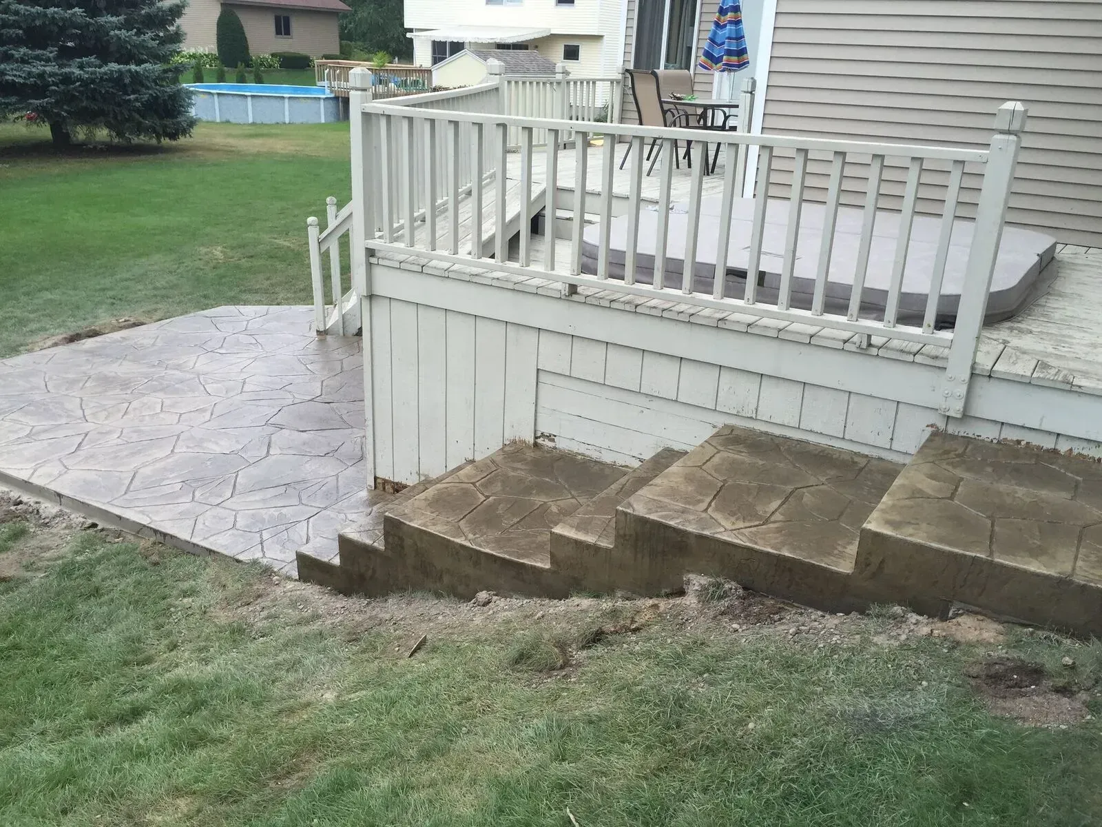 A deck with stairs leading up to it and a pool in the background.