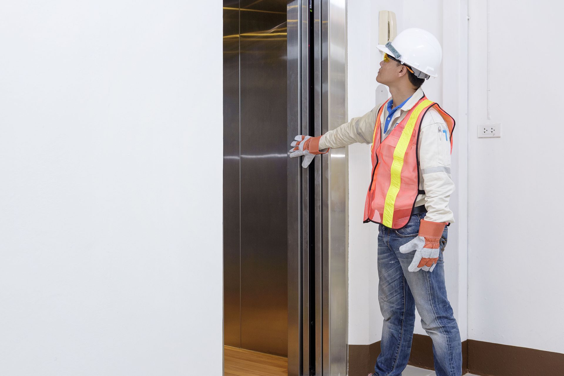 Construction worker opens elevator door in white room.