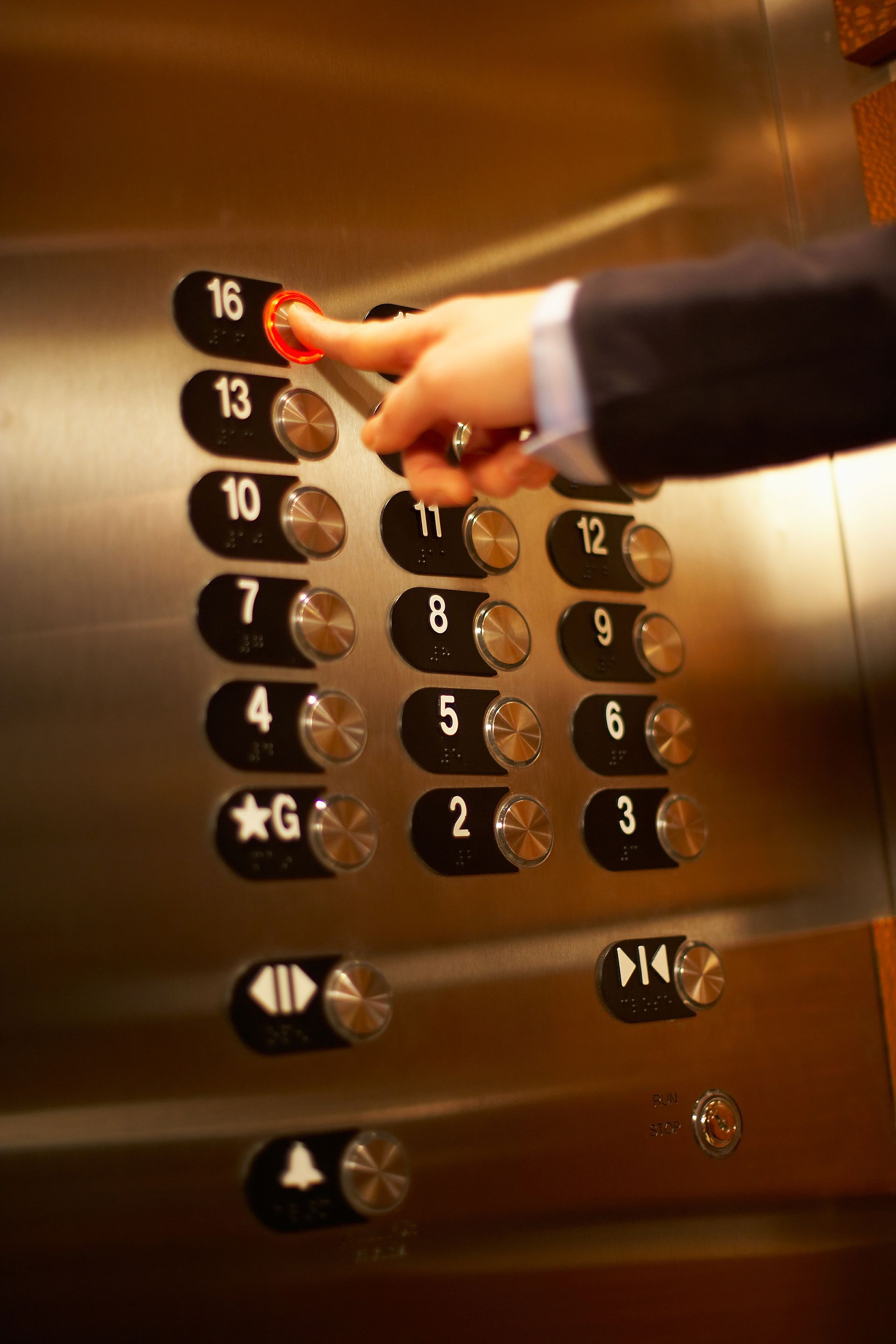 Person in suit presses elevator button for floor 16.