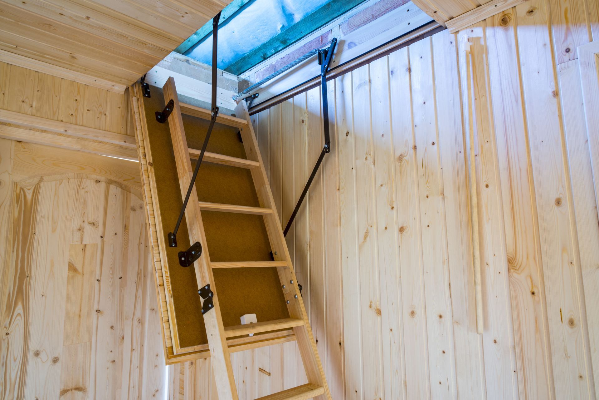 Wooden attic ladder descending from an opening in a wood-paneled ceiling.