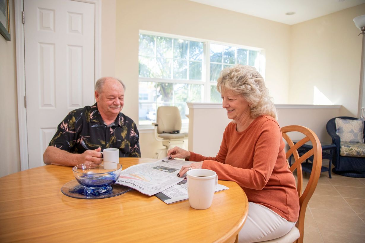 Senior couple at a table, drinking coffee and reading. Smiling in a light-filled room.