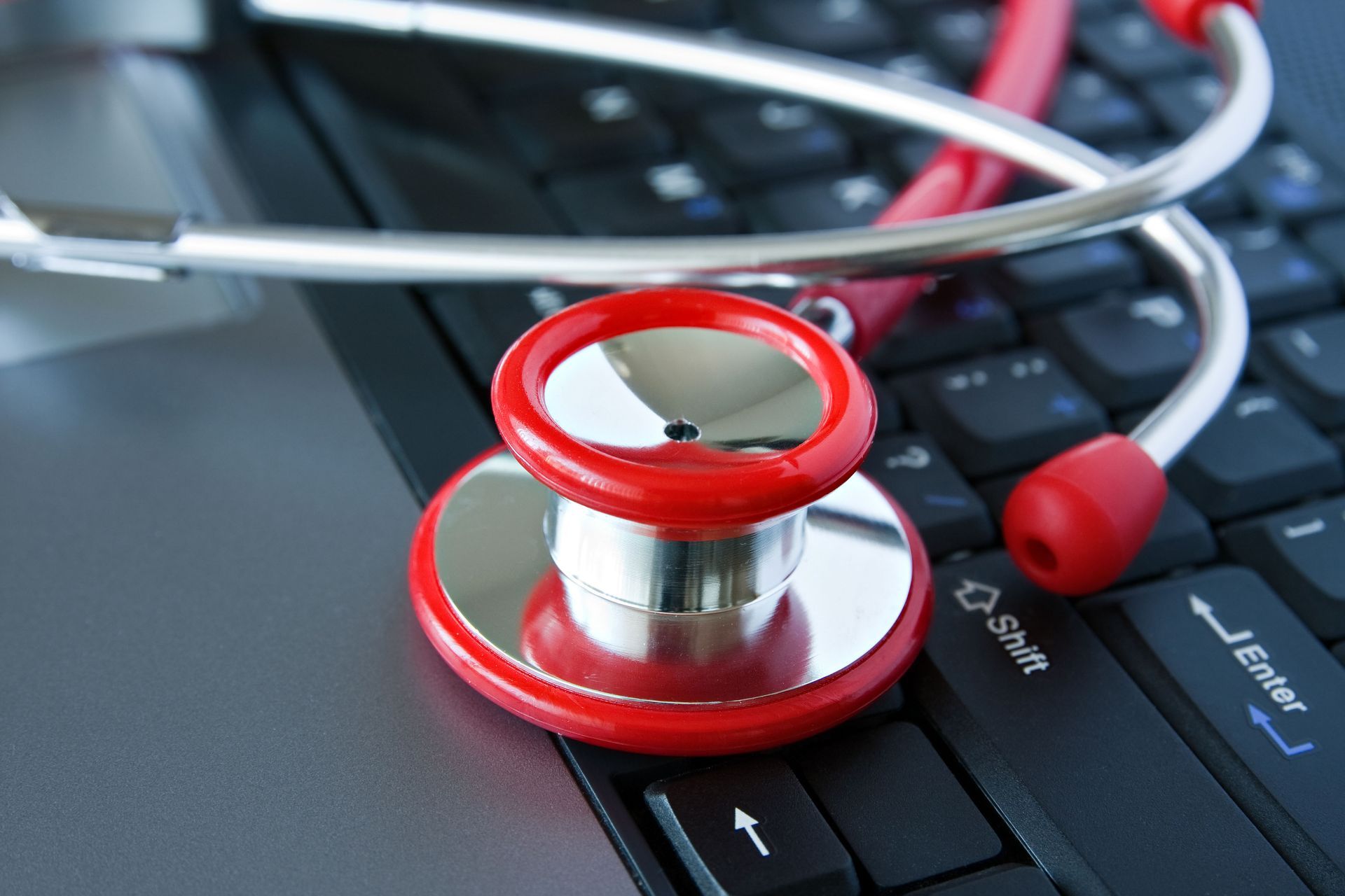 A red stethoscope rests on top of a laptop keyboard