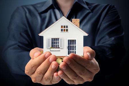 A person is holding a small white house in their hands