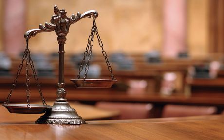 A scale of justice sits on a wooden table in a courtroom