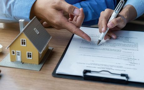 A person is signing a document next to a model house.