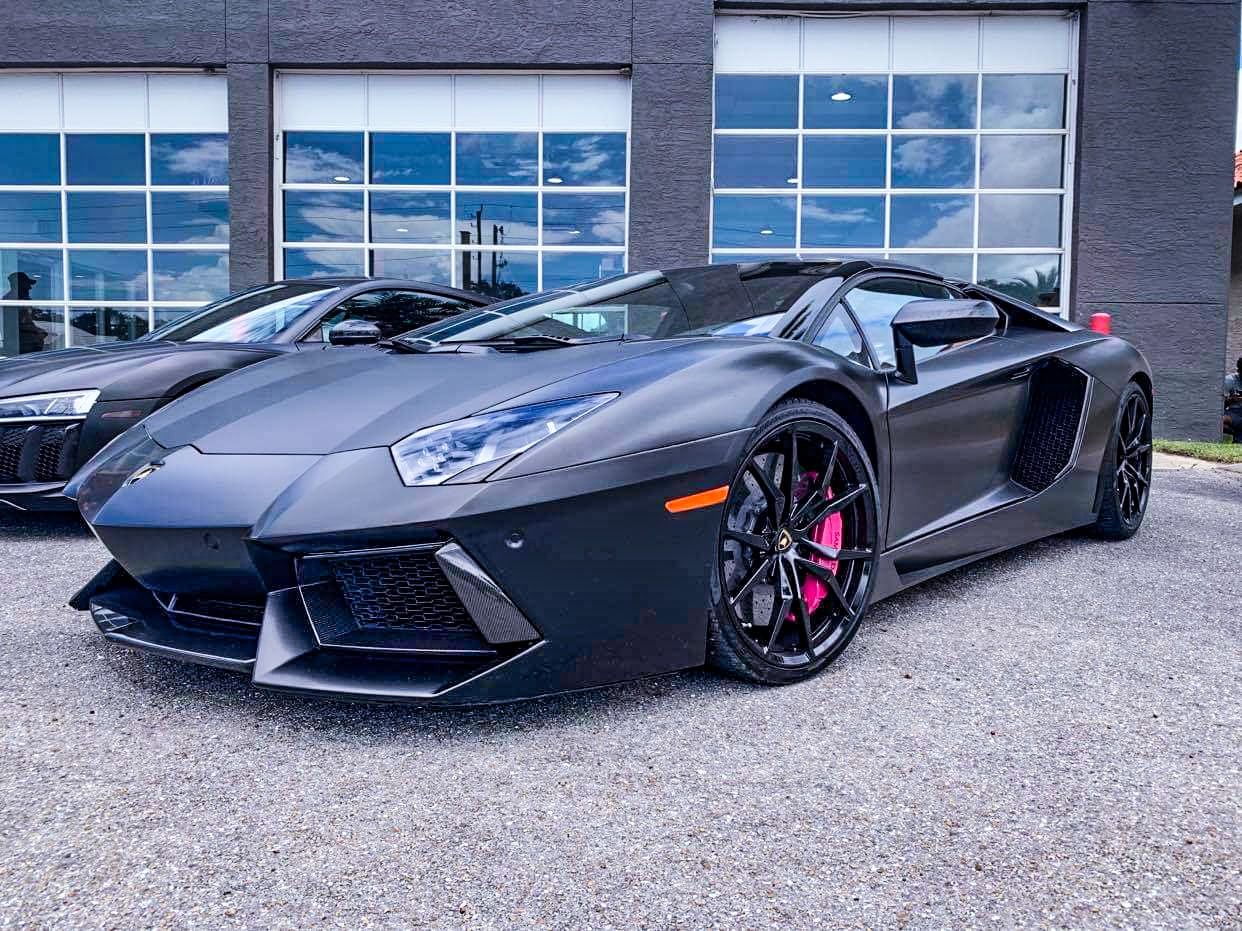 Black Lamborghini Aventador with pink brake calipers parked outside a building.