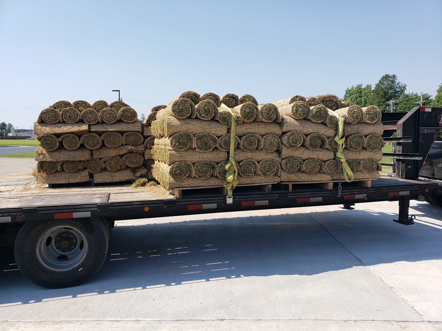 A truck is loaded with rolls of grass on a trailer
