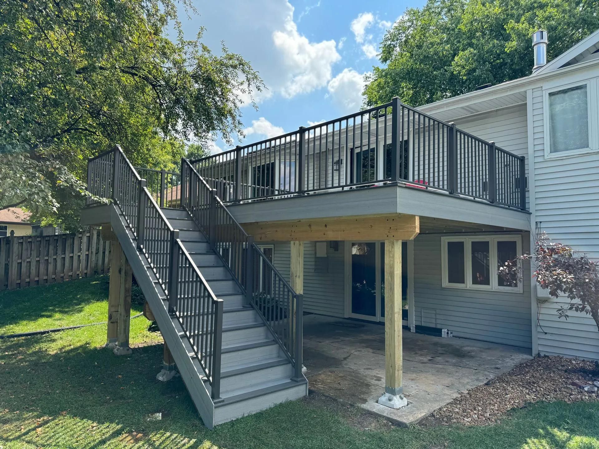 A large deck with stairs leading up to it is in the backyard of a house.