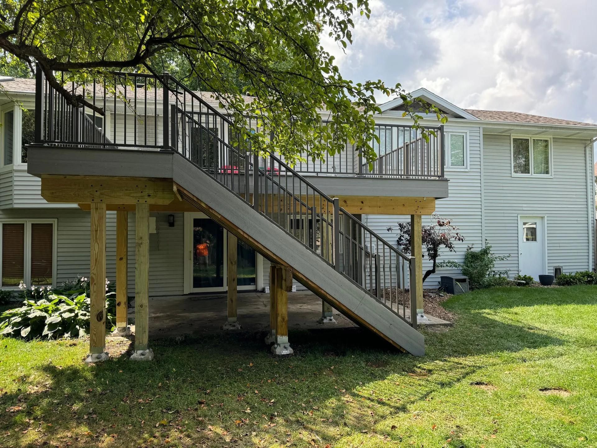 A large deck with stairs leading up to it is in the backyard of a house.