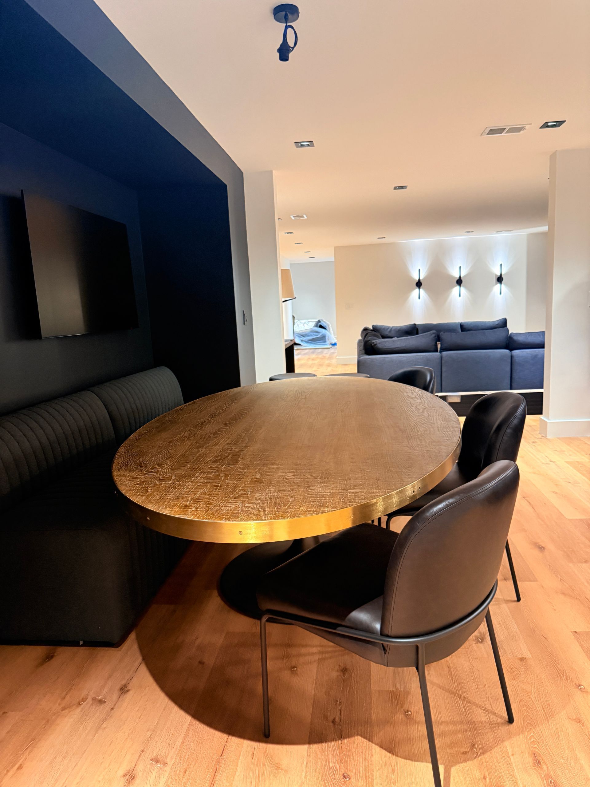 Modern dining area with oval wooden table, black chairs, and a dark sofa in an open-plan living room.