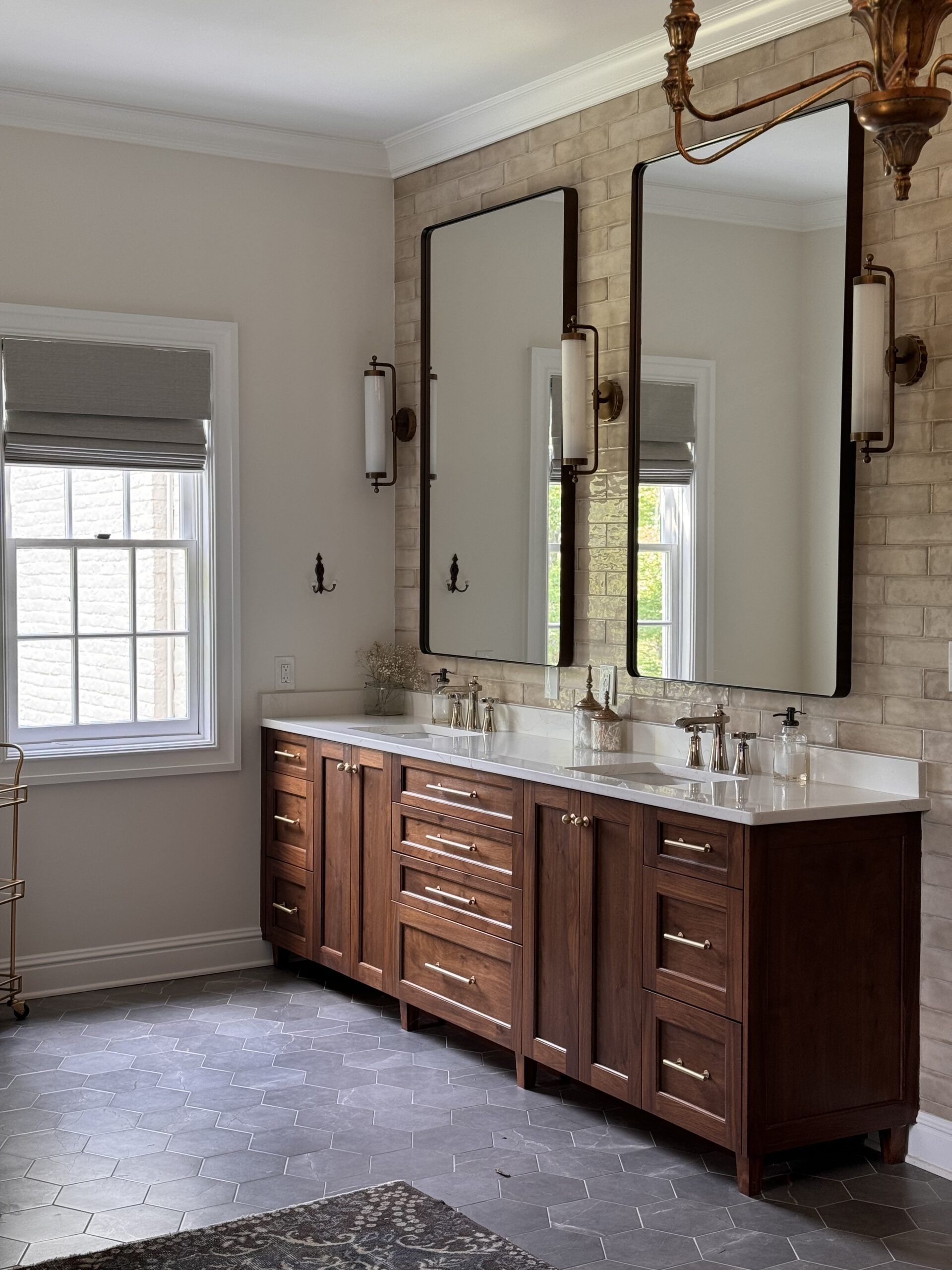 Bathroom with double vanity, large mirrors, marble countertop, and window with white shade.