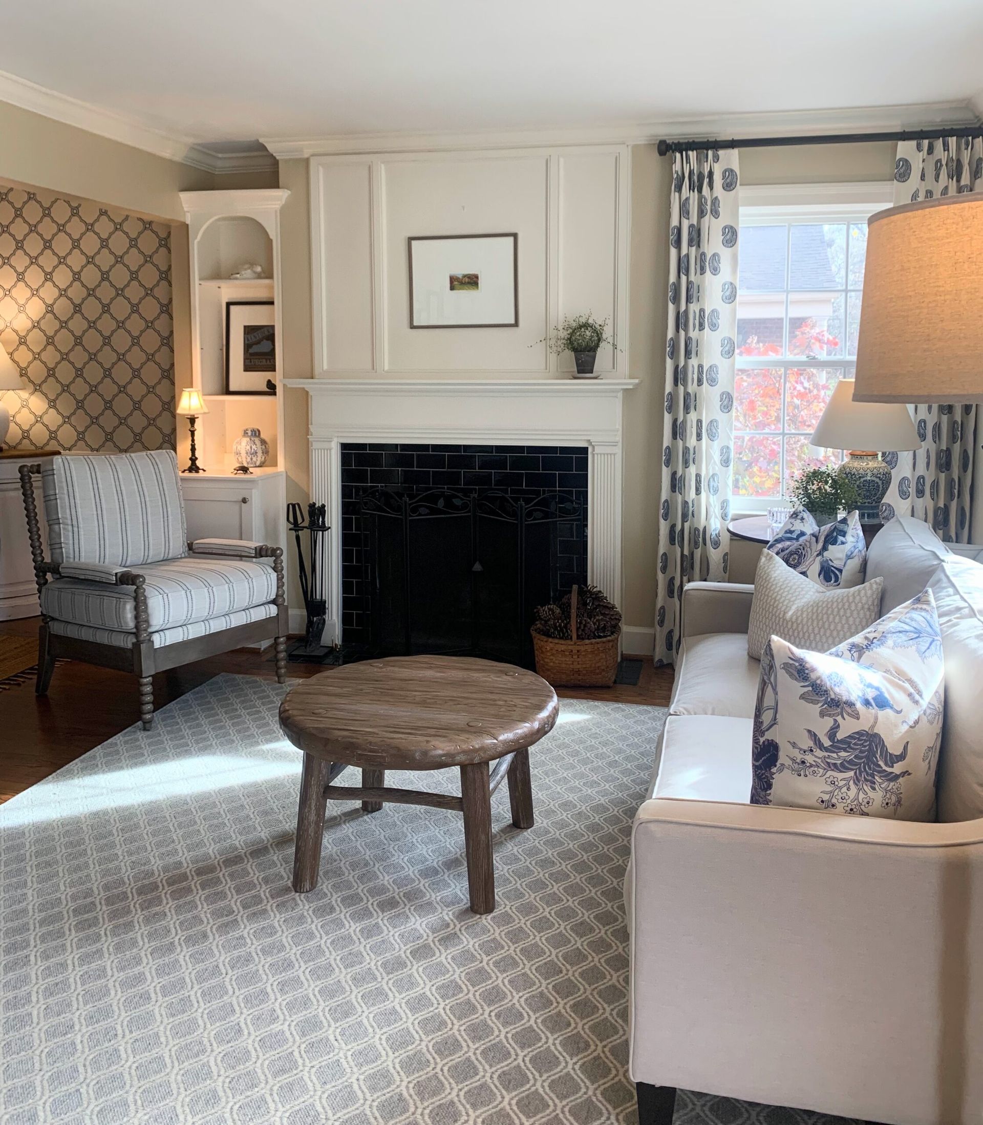 Bright living room with fireplace, patterned chairs, sofa, round coffee table, and large window.