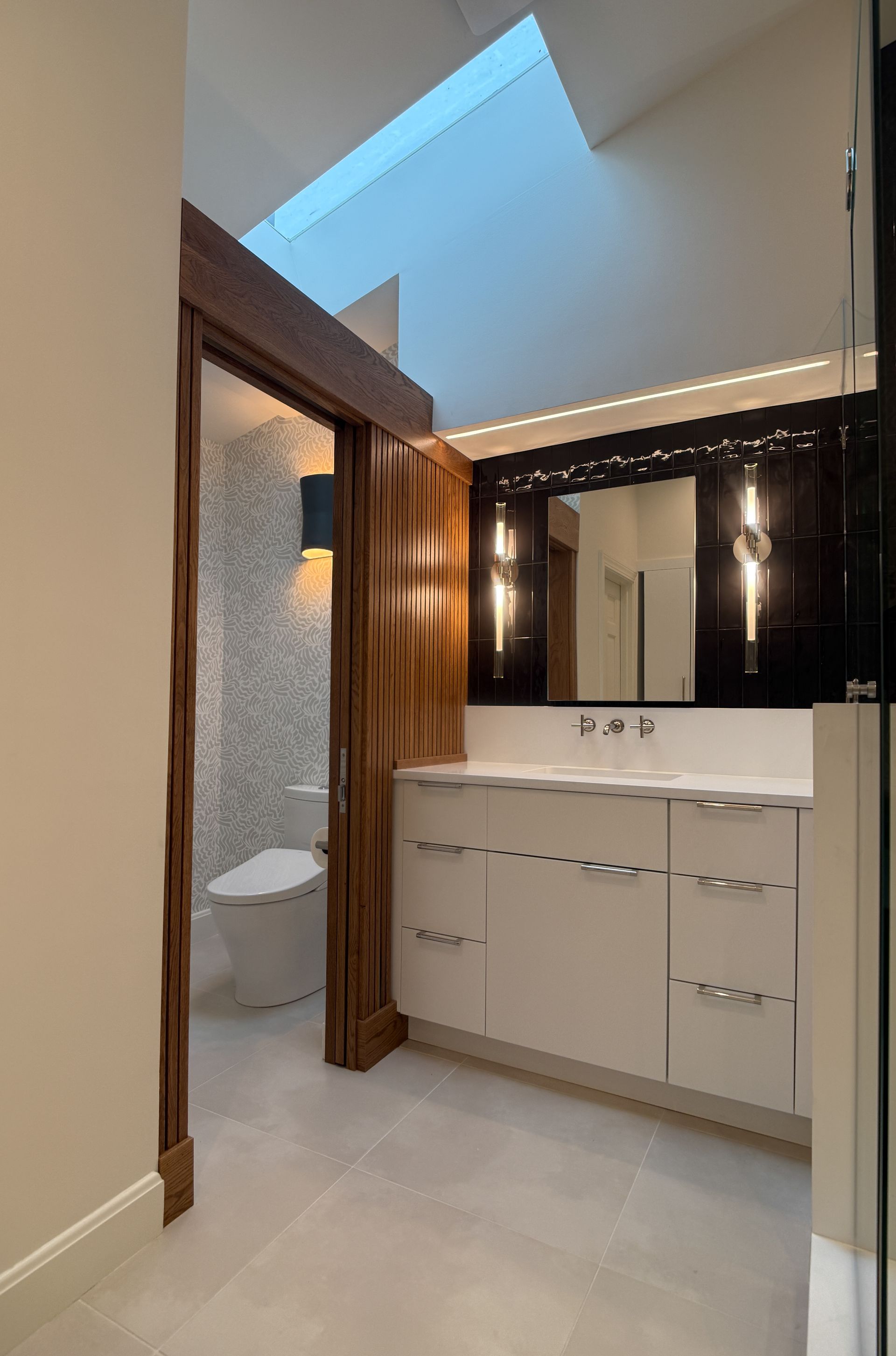 Modern bathroom vanity with mirror, white cabinets, dark wood trim, and a skylight overhead.