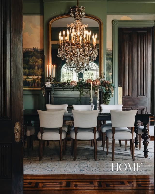 Elegant dining room with crystal chandelier, white chairs, dark wood table, and large mirror above a fireplace.