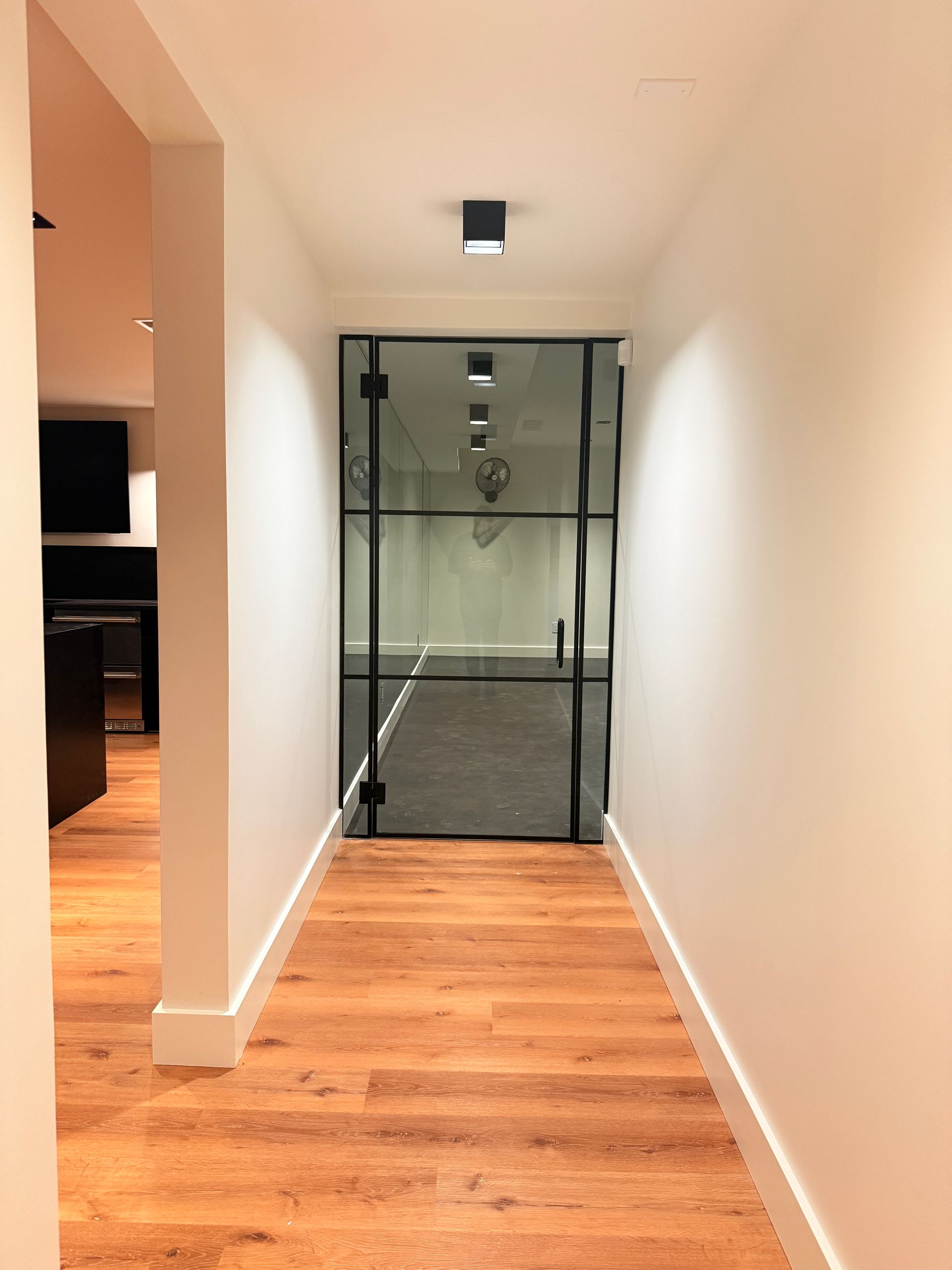 Hallway with wood floor leading to a glass door and a white staircase railing on the left.