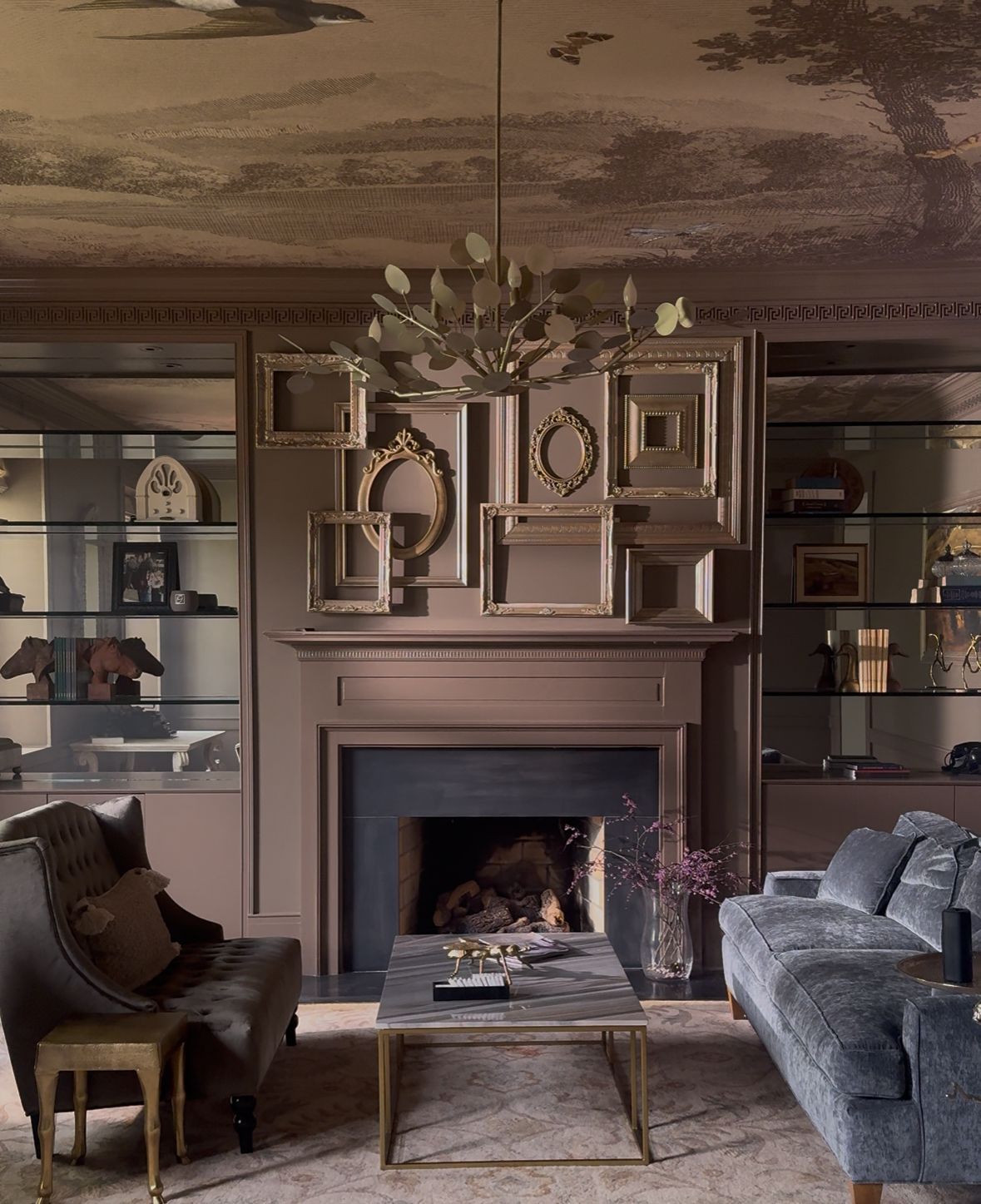 Elegant living room with fireplace, ornate mantel, chandelier, and blue and brown armchairs.