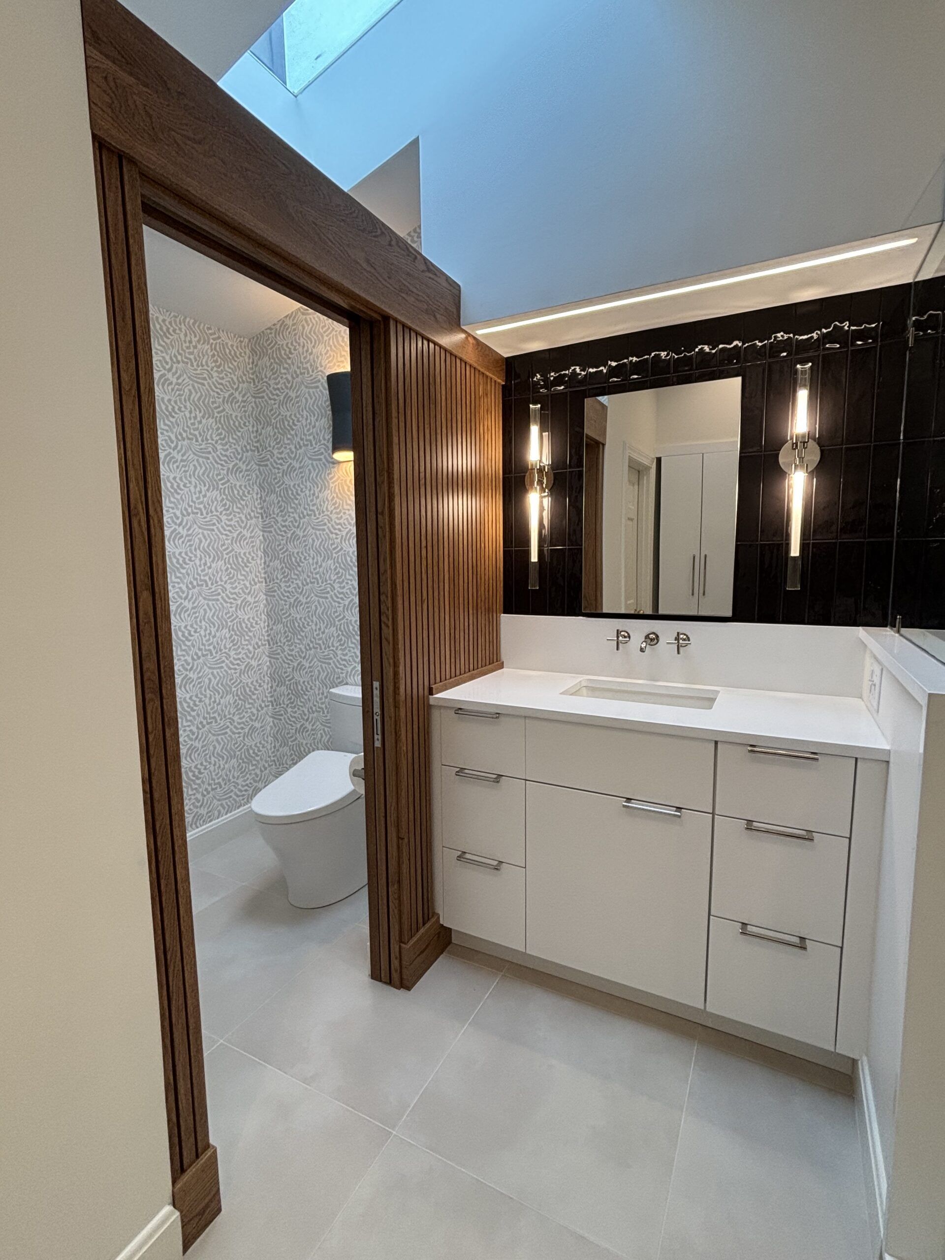 Modern bathroom vanity with mirror, white cabinet, and glass-enclosed shower with wood trim.