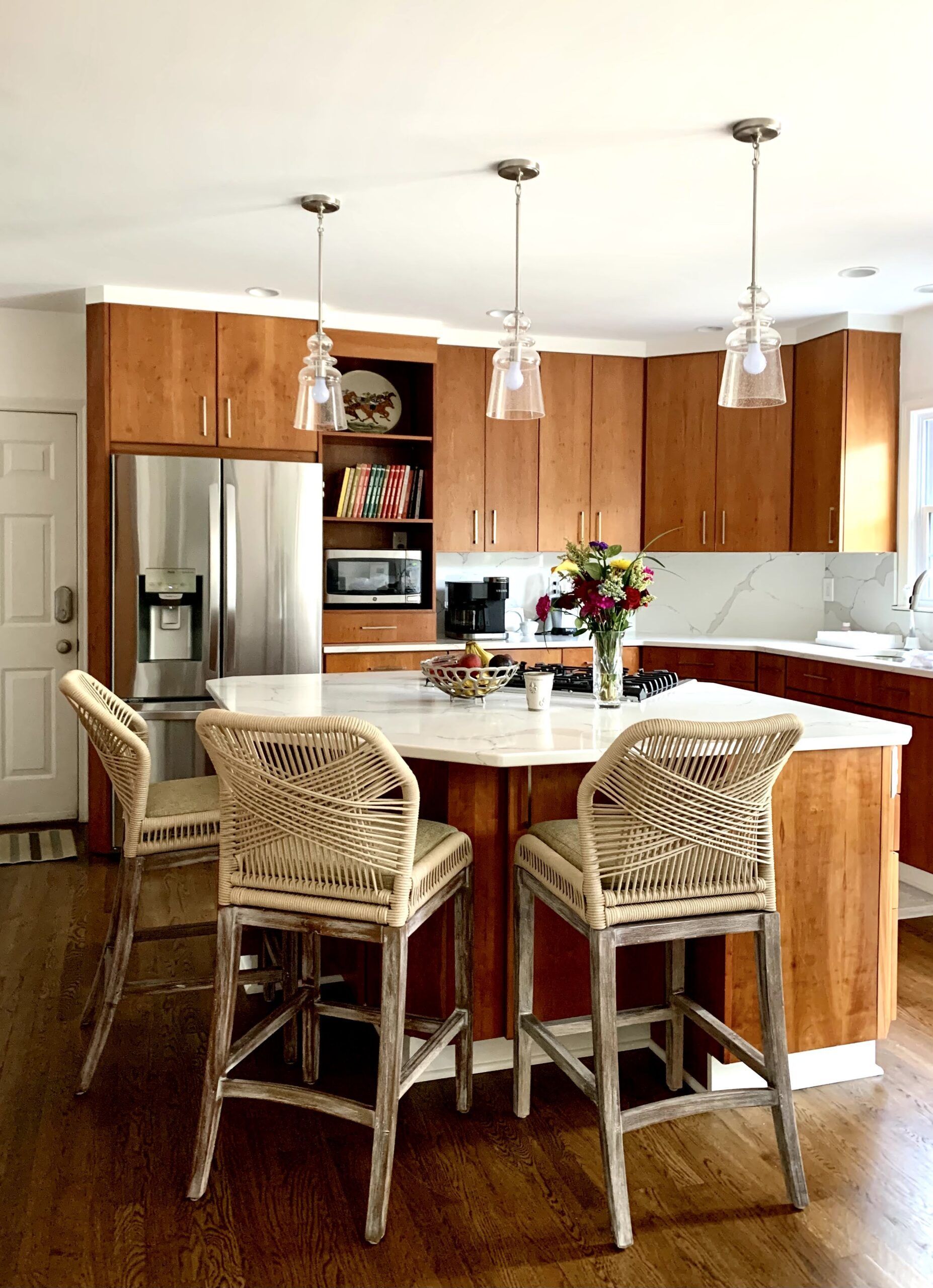 Bright kitchen with a white island, wicker bar stools, wood cabinets, and stainless steel appliances.