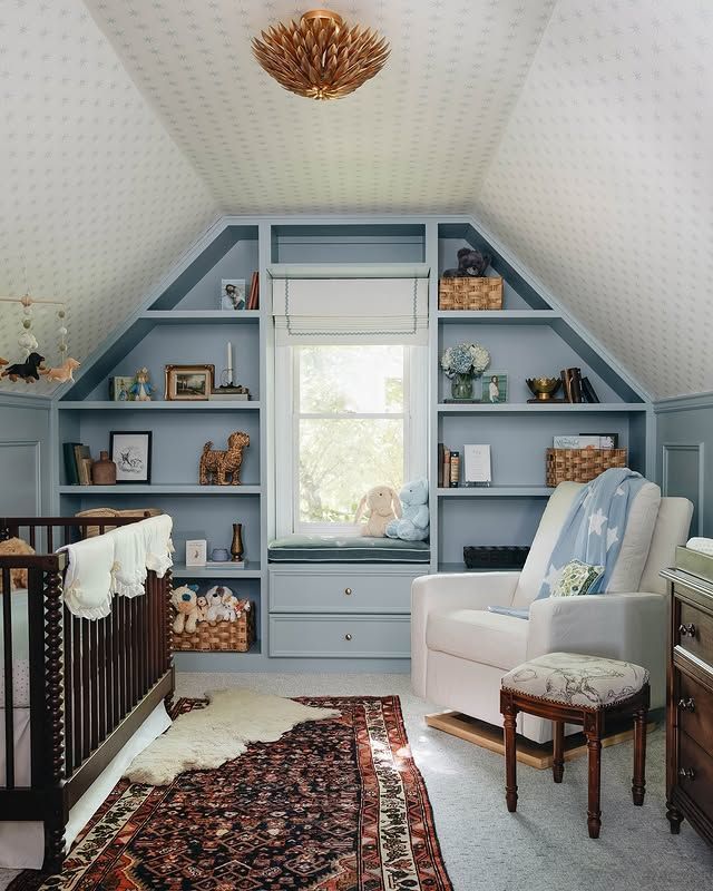 Cozy blue attic nursery with built-in shelves, crib, chair, window, and patterned rug.