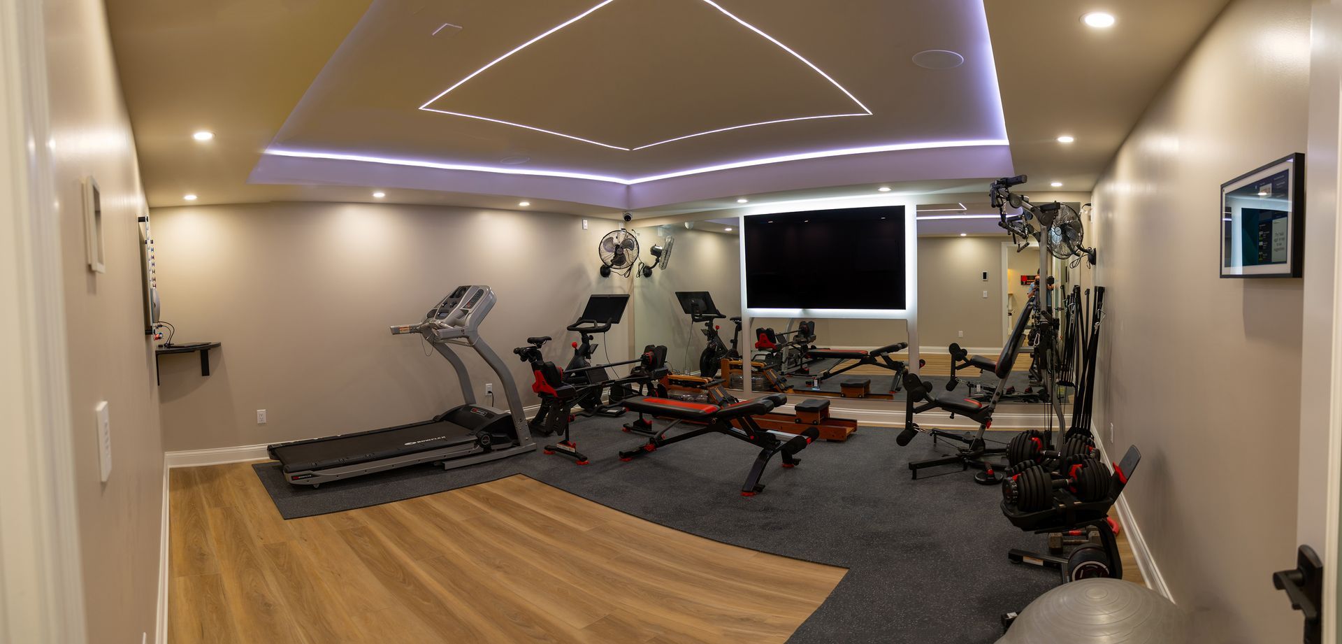 Modern home gym with exercise bikes, treadmill, weights, and wall-mounted TV in a sleek room
