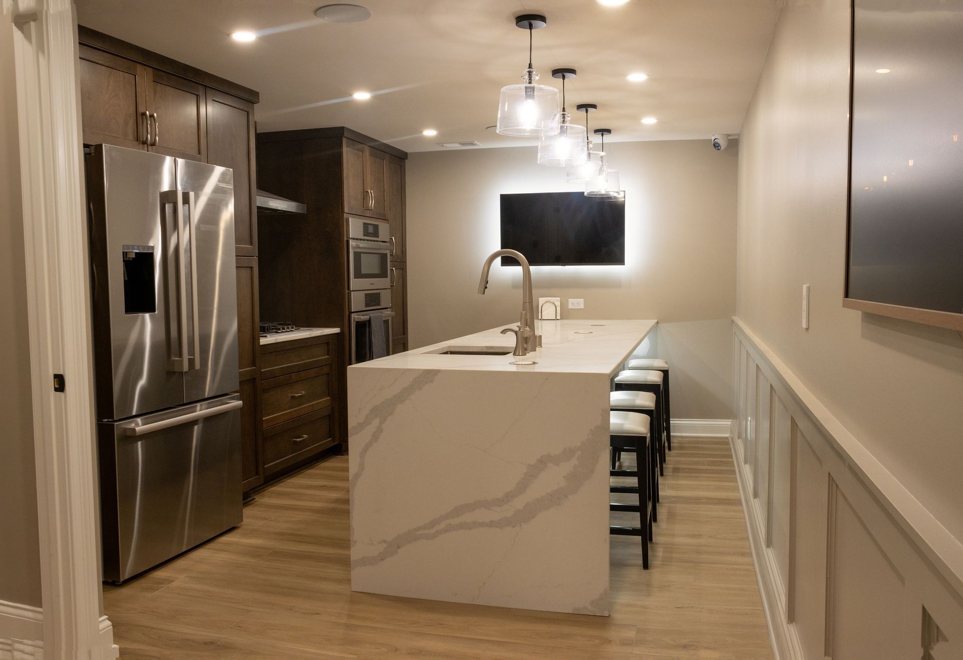 Modern kitchen with stainless steel fridge, marble island, pendant lights, and bar stools