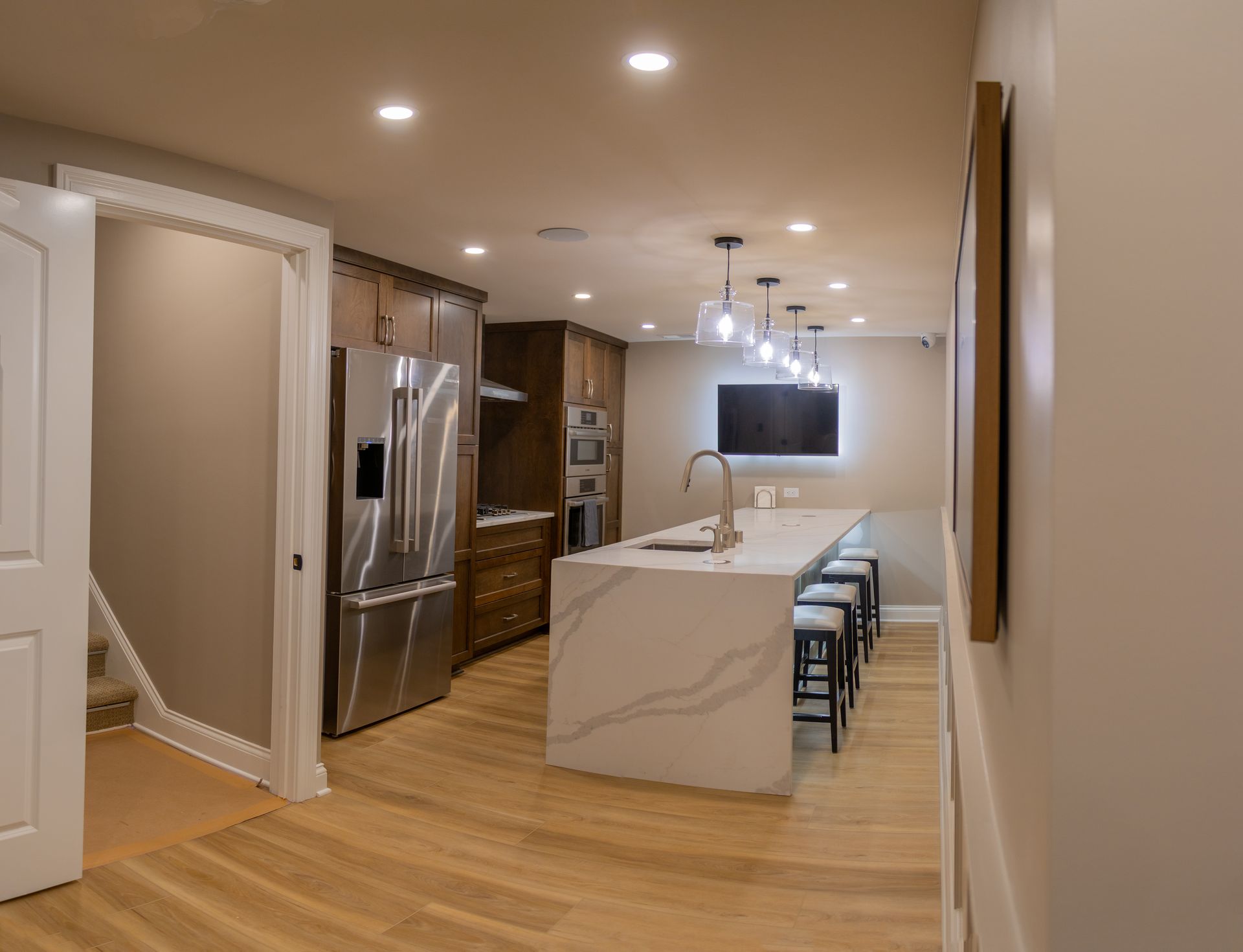 Modern kitchen with marble island, stainless appliances, wood floors, and bar stools under recessed lighting