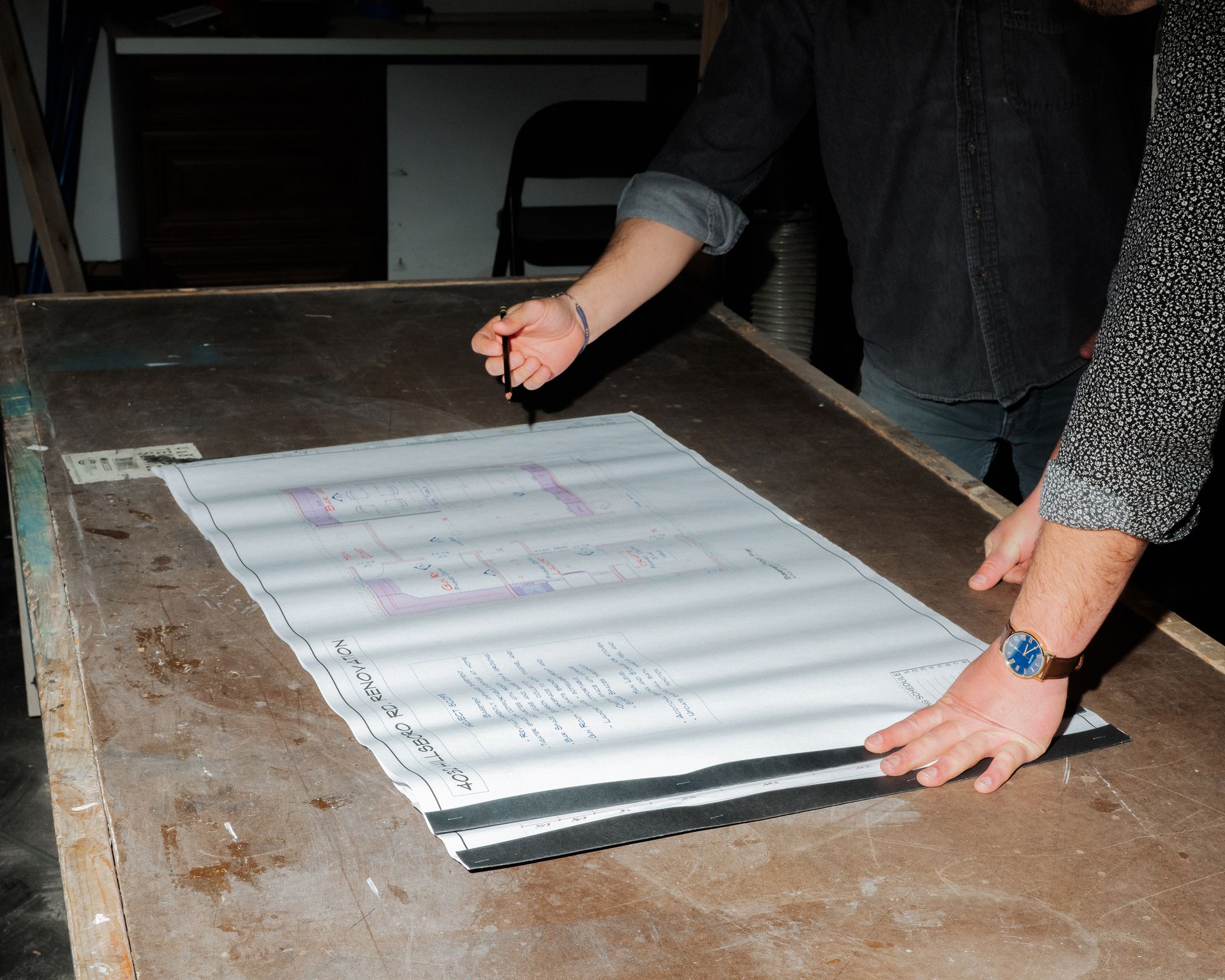Two people handling a large white sheet on a worn wooden table in a workshop