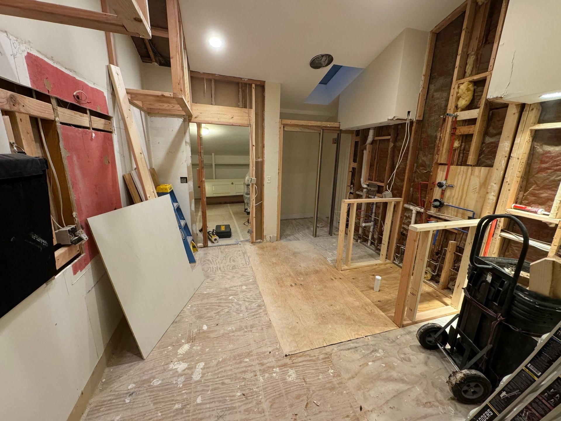 Renovation site with exposed framing, drywall panels, and tools in a partially gutted room