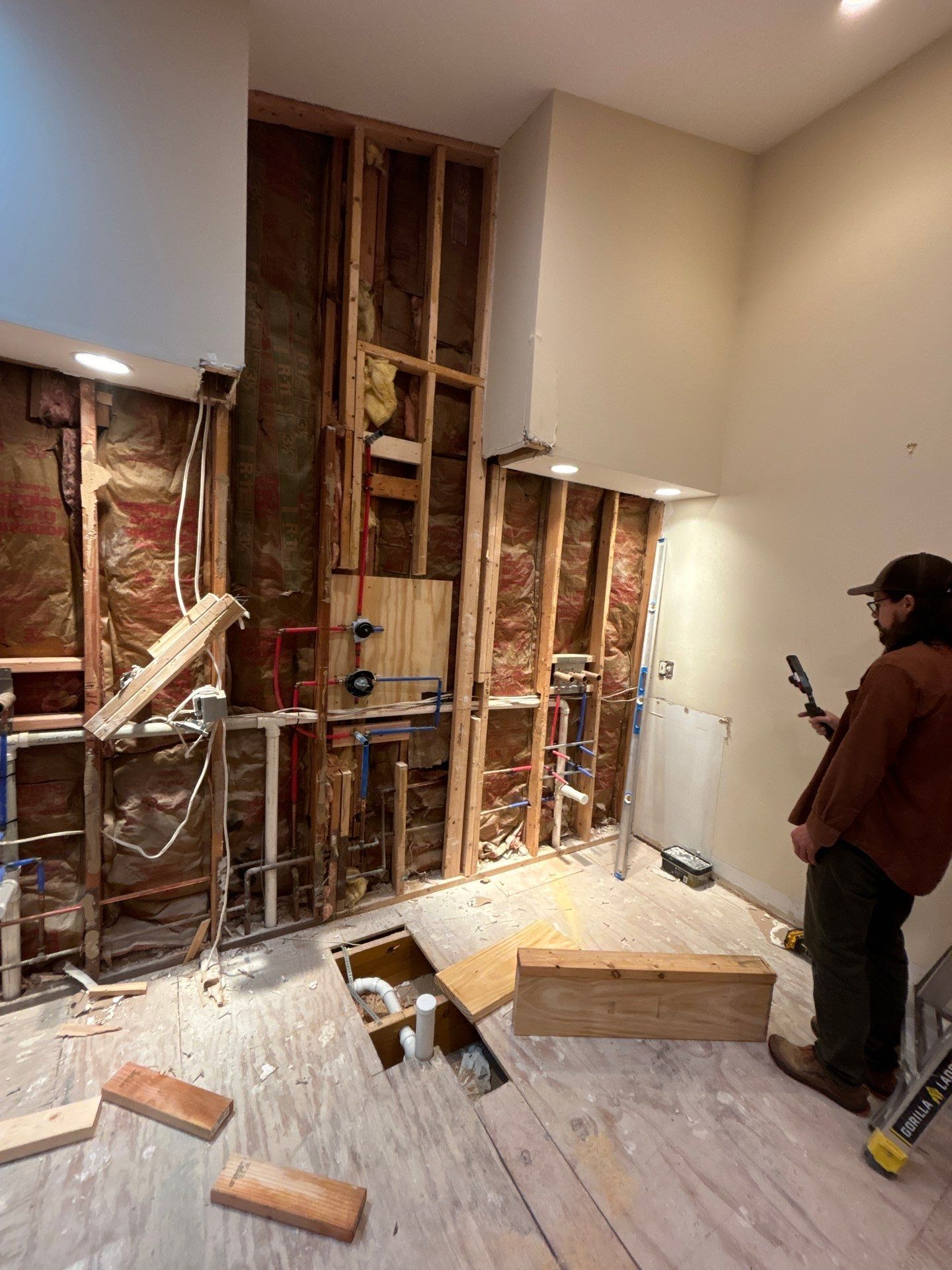 Partially demolished room with exposed studs and debris; a person stands on the right holding a phone.