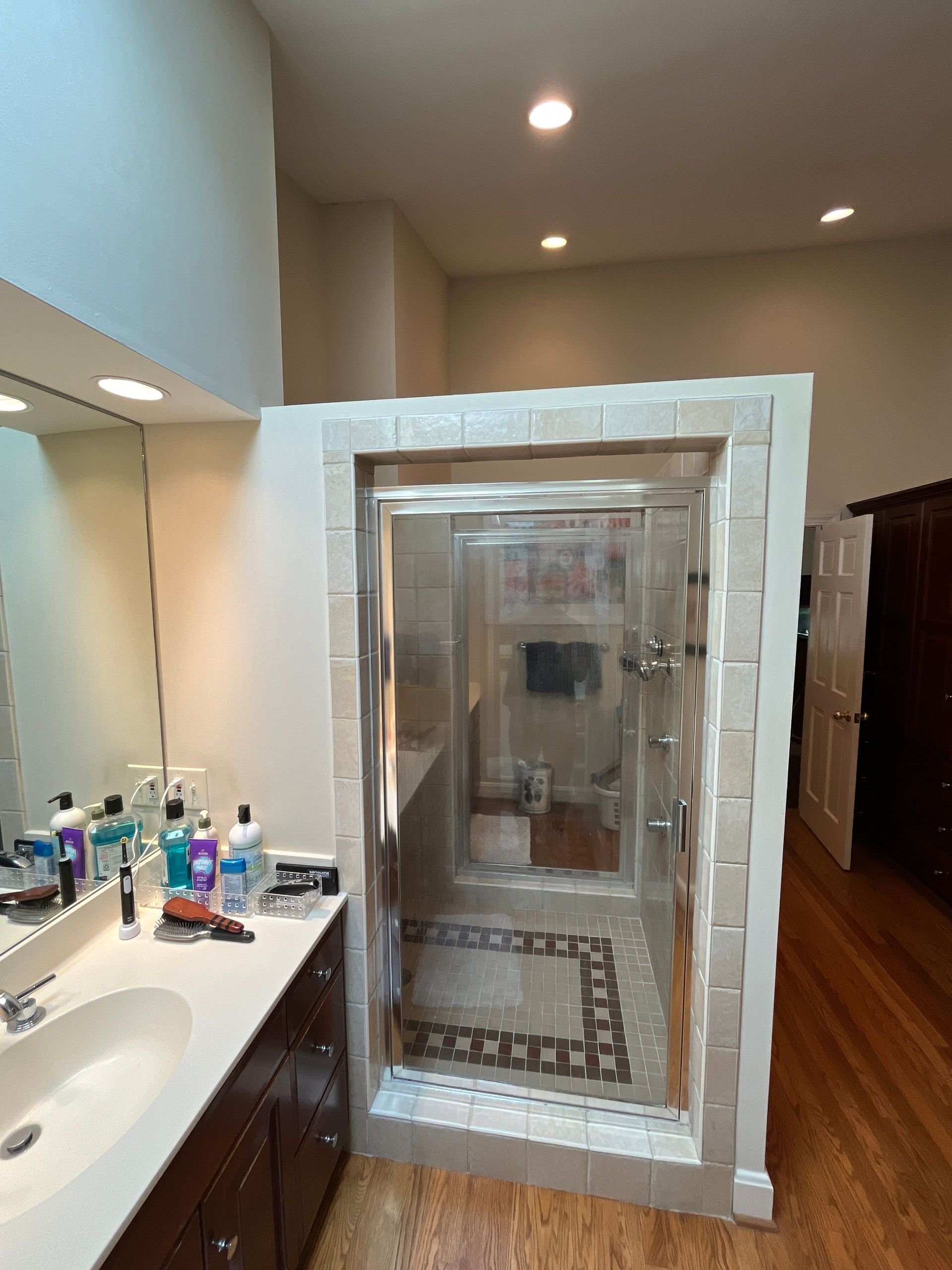 Bathroom with white-tiled shower enclosure beside a sink vanity and wooden floor