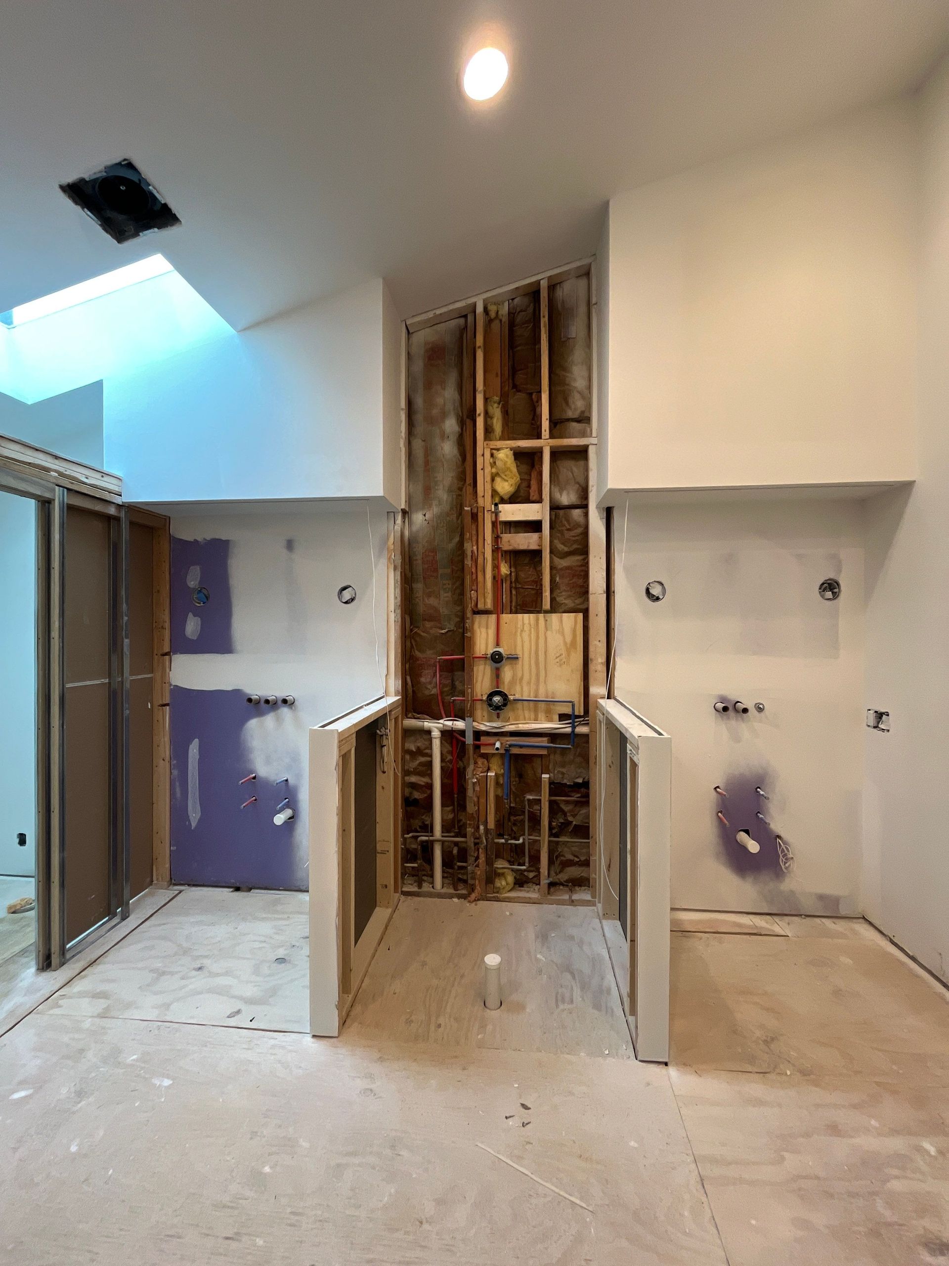 Partially renovated room with exposed framing, drywall, and a skylight opening