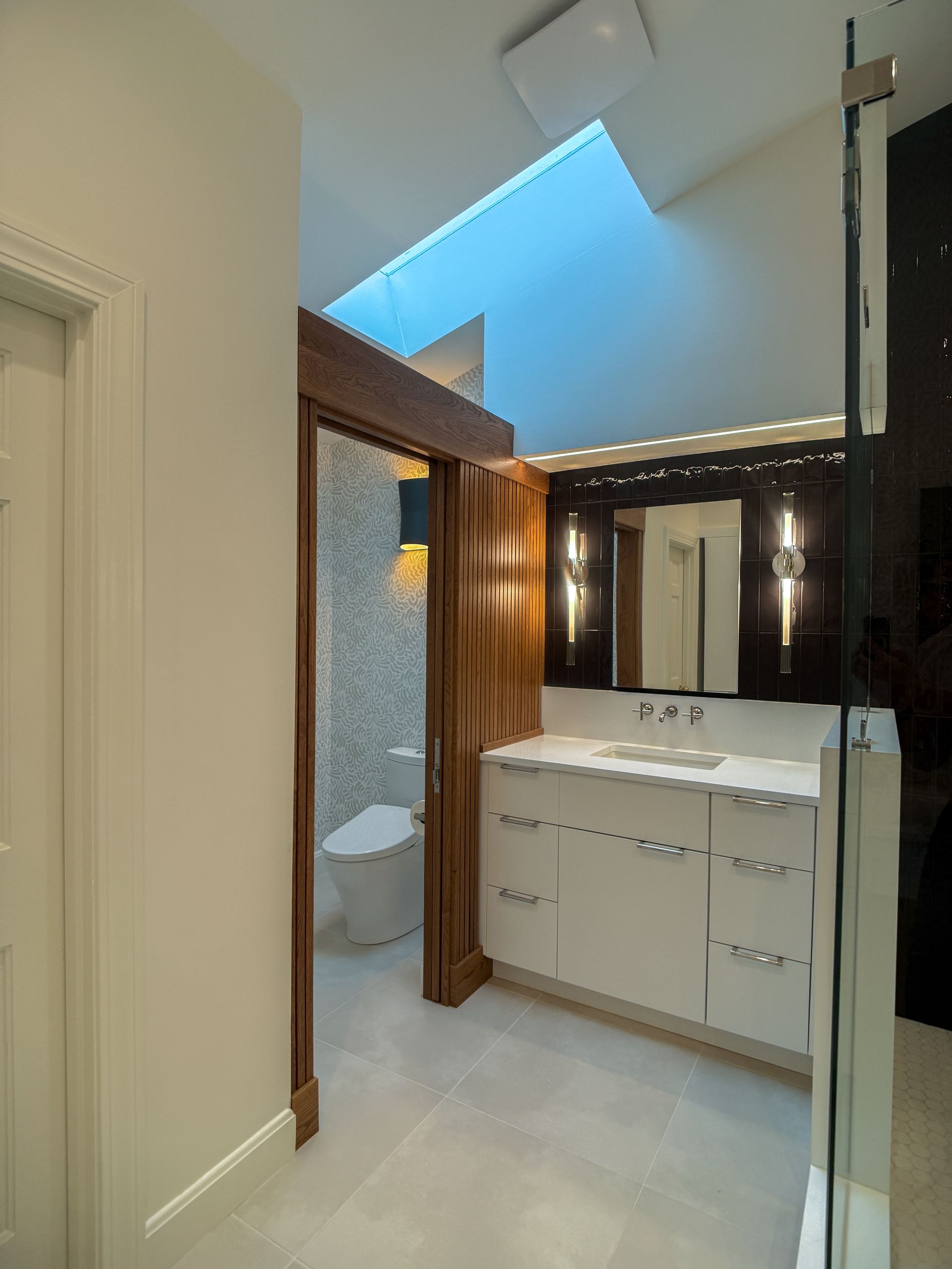 Modern bathroom with skylight, frosted shower enclosure, wood accents, and white vanity sink.