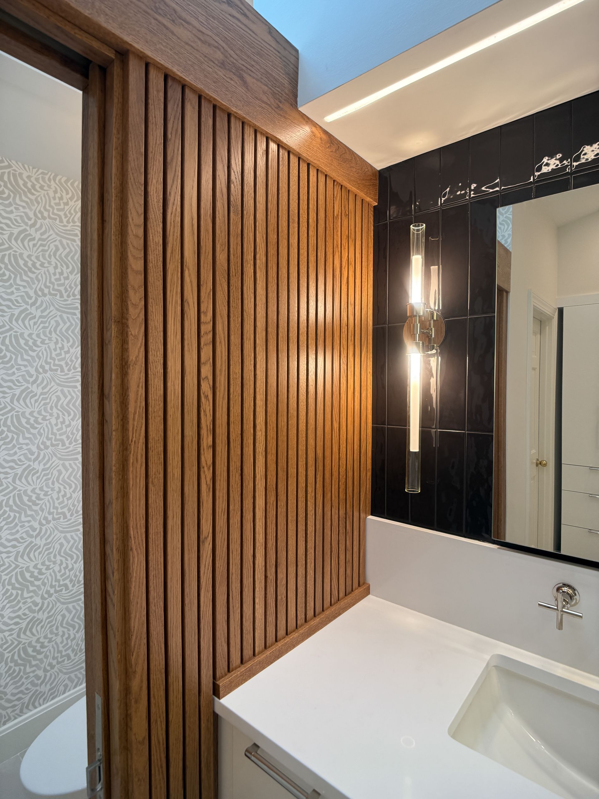 Bathroom vanity with wood slat wall, mirror, and white sink beneath warm lighting