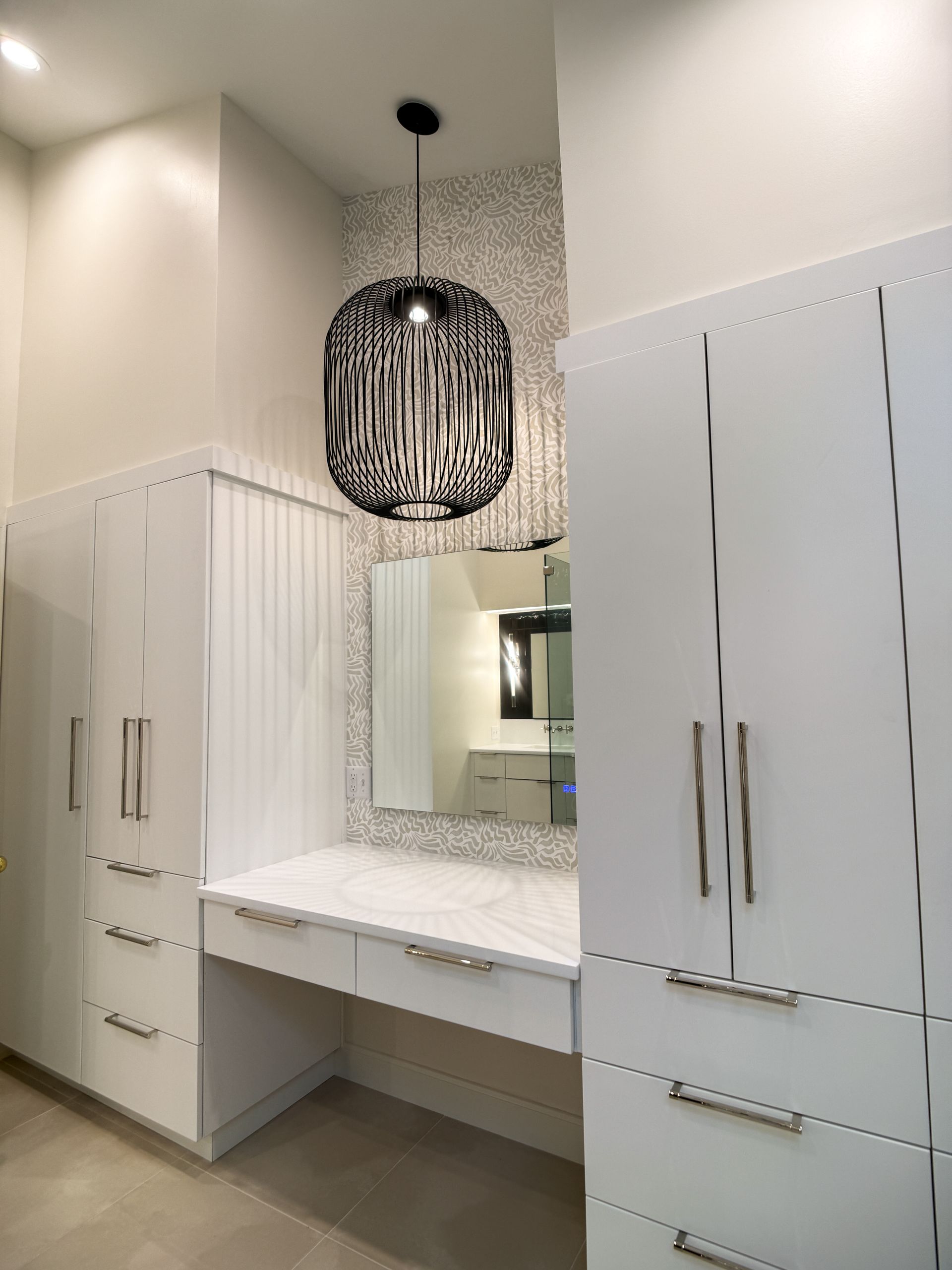 Modern white vanity area with mirror, built-in cabinets, and black pendant light in a bright room