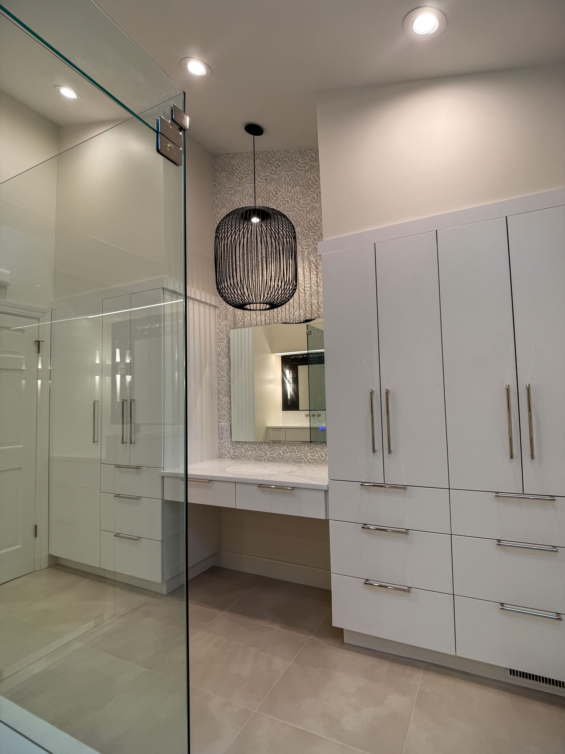 Modern bathroom with white cabinets, glass shower, vanity, and black pendant light