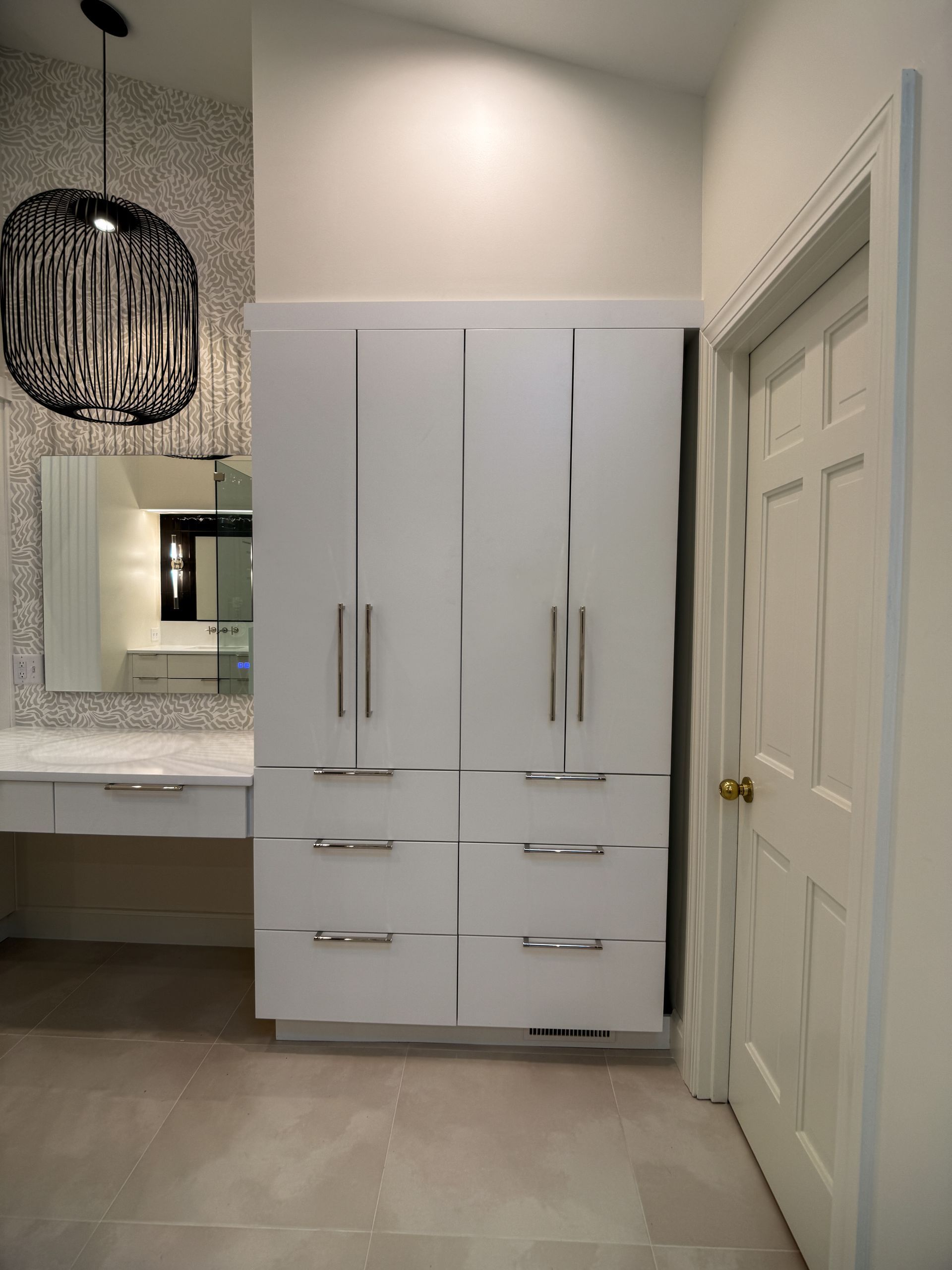 Modern white bathroom vanity and storage cabinet beside a closed door in a tiled room.