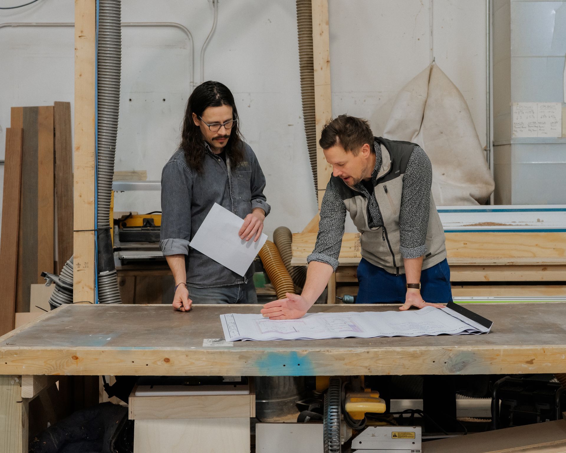 Two people reviewing plans on a large worktable in a workshop