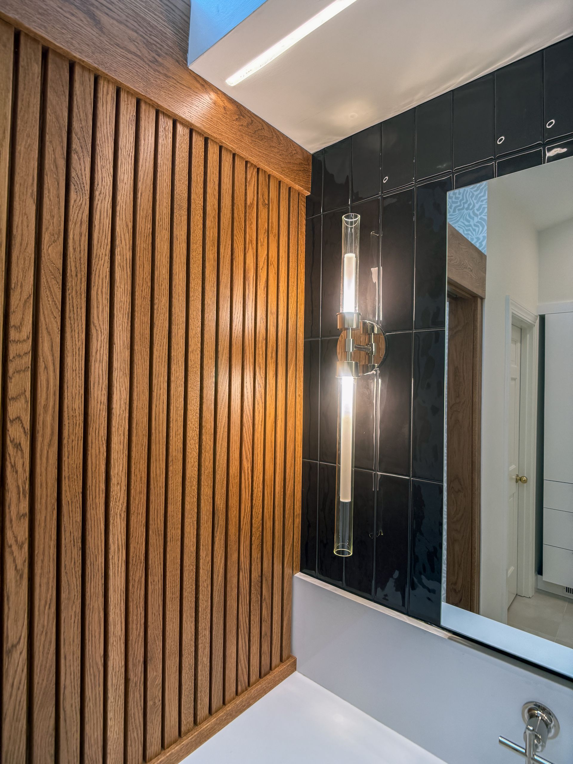 Modern bathroom corner with wood slat wall, glossy black cabinet, sink, and mirror light fixture