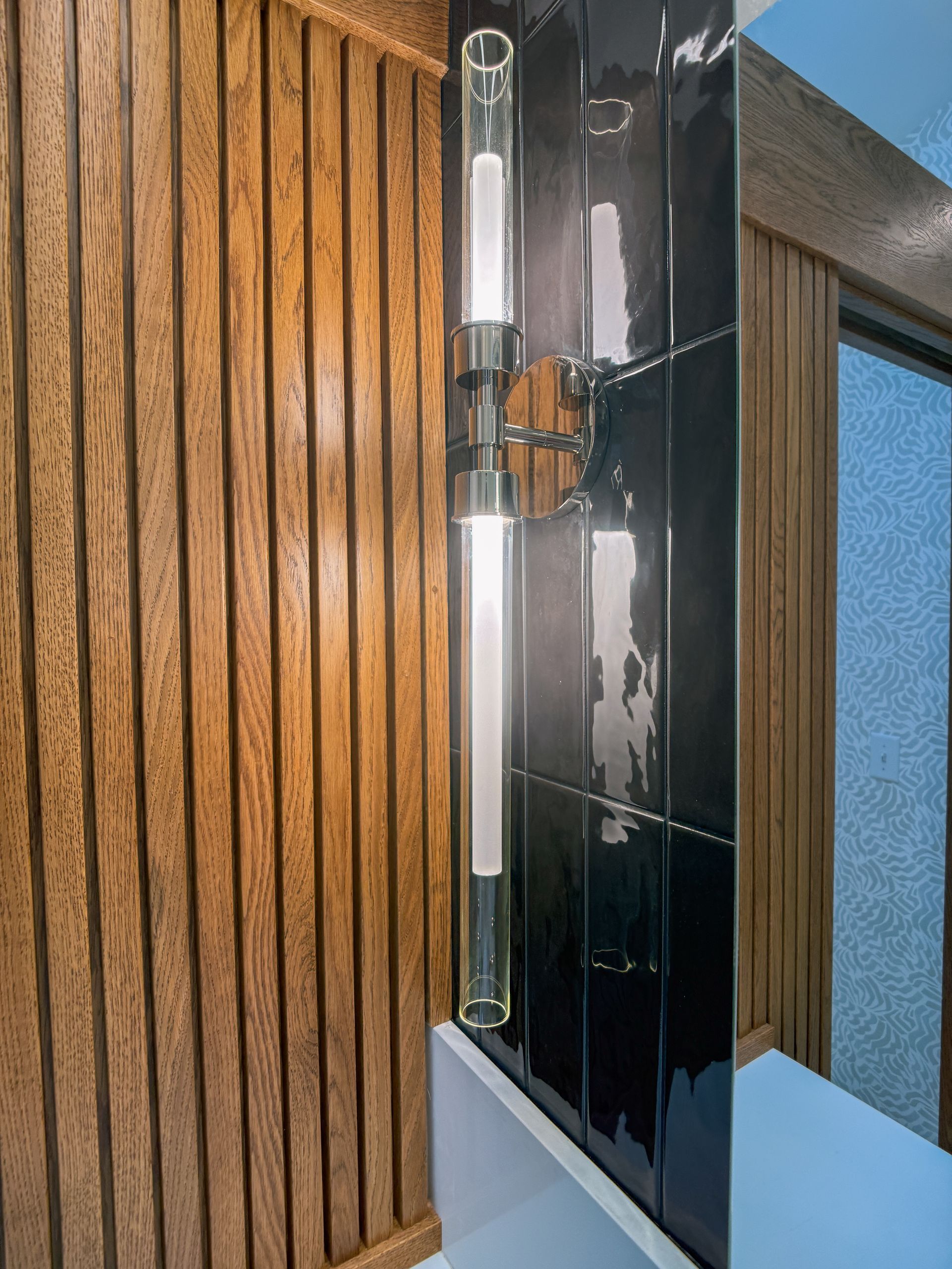 Modern wall sconce with black glass and chrome mounted beside vertical wood paneling