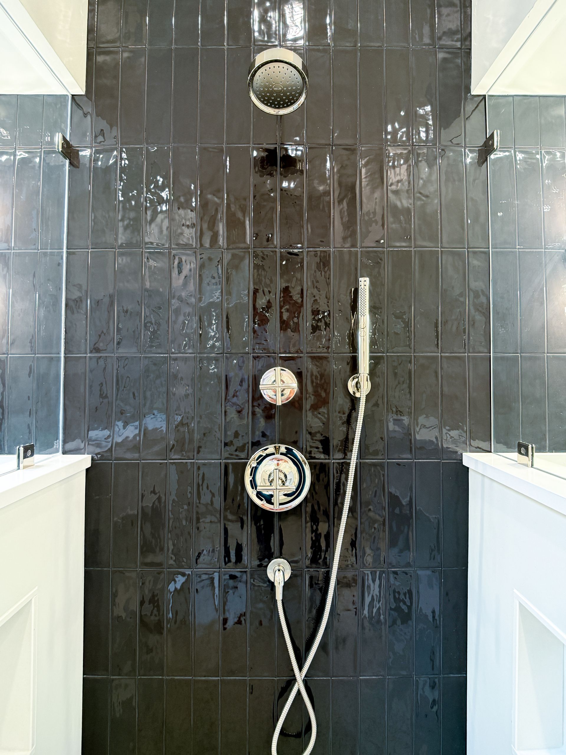 Modern shower stall with dark glossy tiles, white fixtures, and handheld showerhead