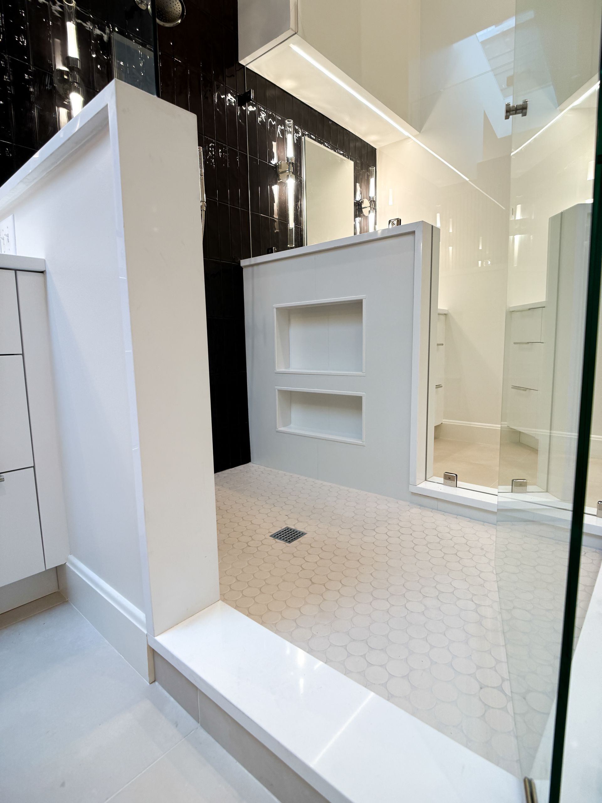 Modern white-tiled bathroom with a glass shower, built-in shelf, and black accent wall display.