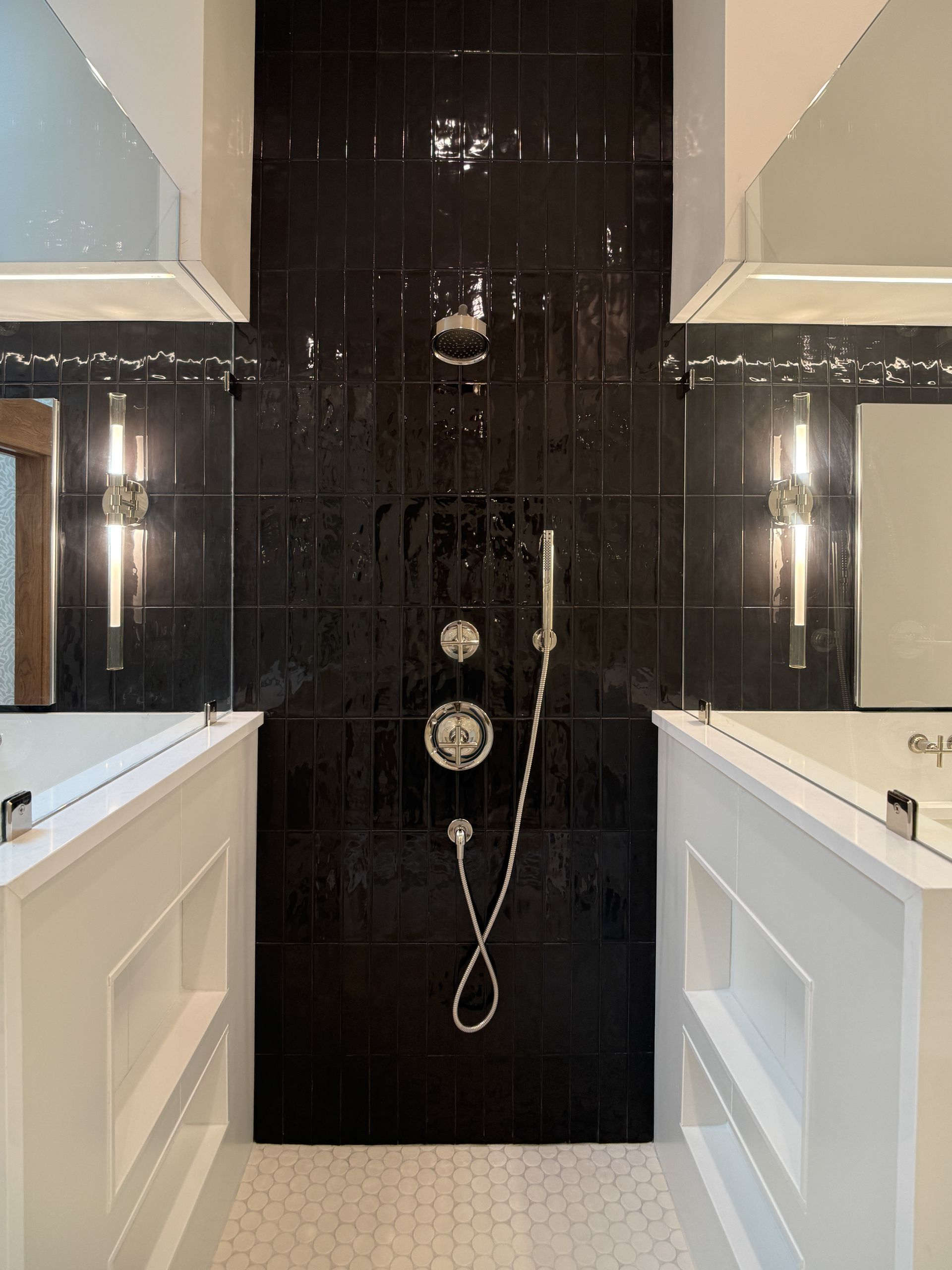 Modern bathroom with black tiled shower wall, white vanities, and chrome fixtures in a symmetrical layout