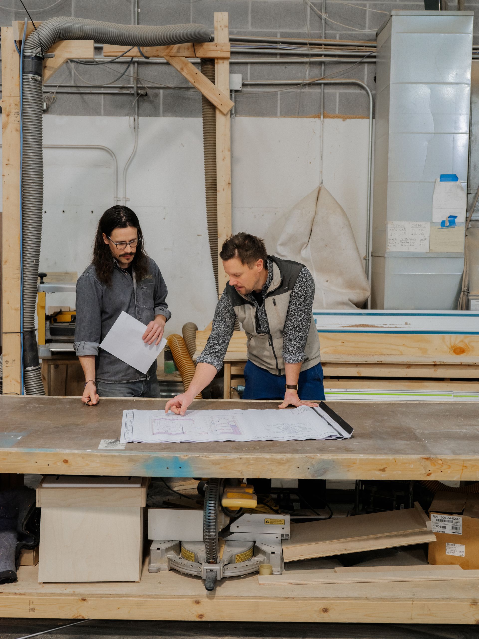 Two people reviewing plans at a workbench in a construction workshop