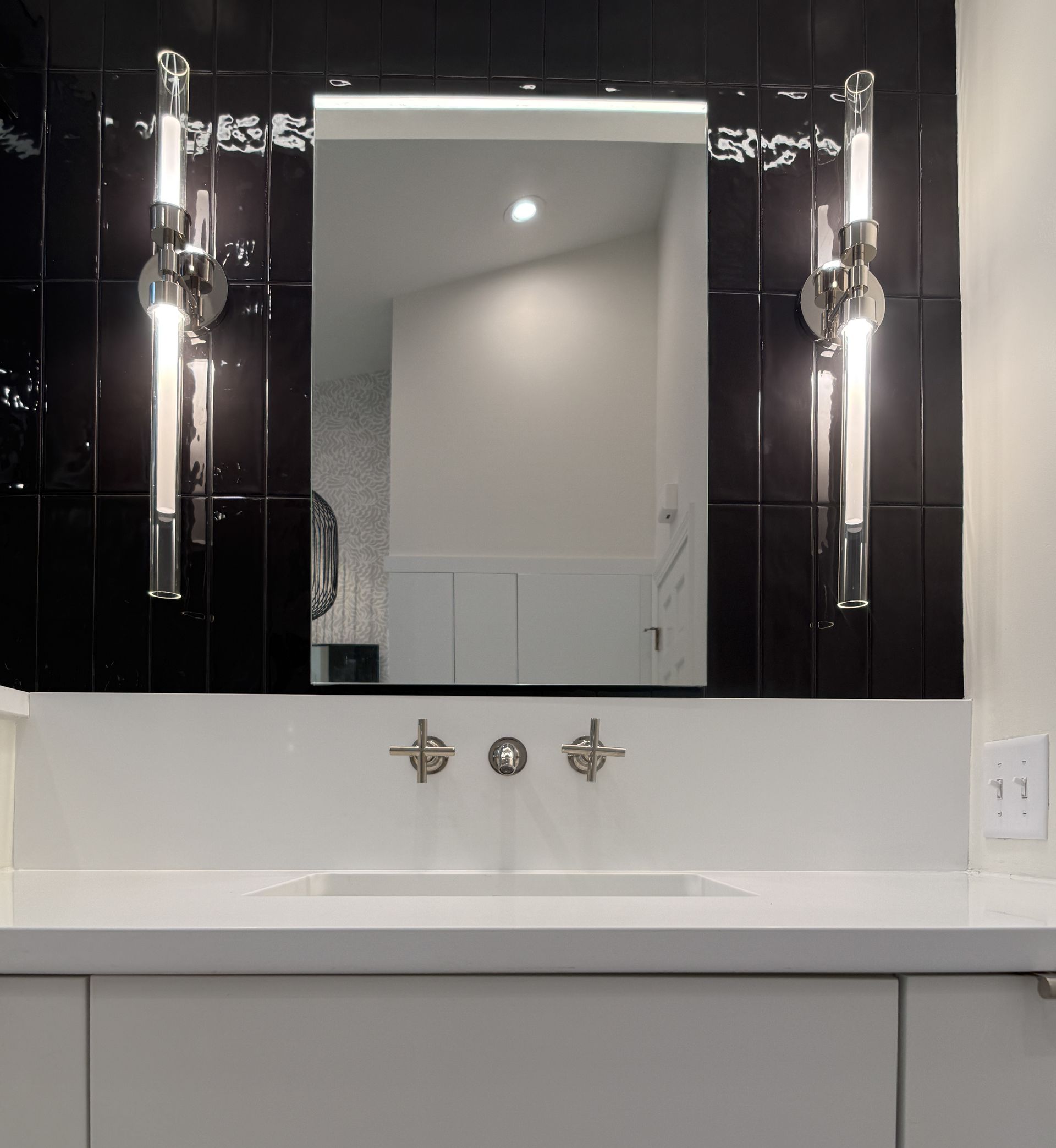Bathroom vanity with large mirror, white sink, and black side panels reflecting the room