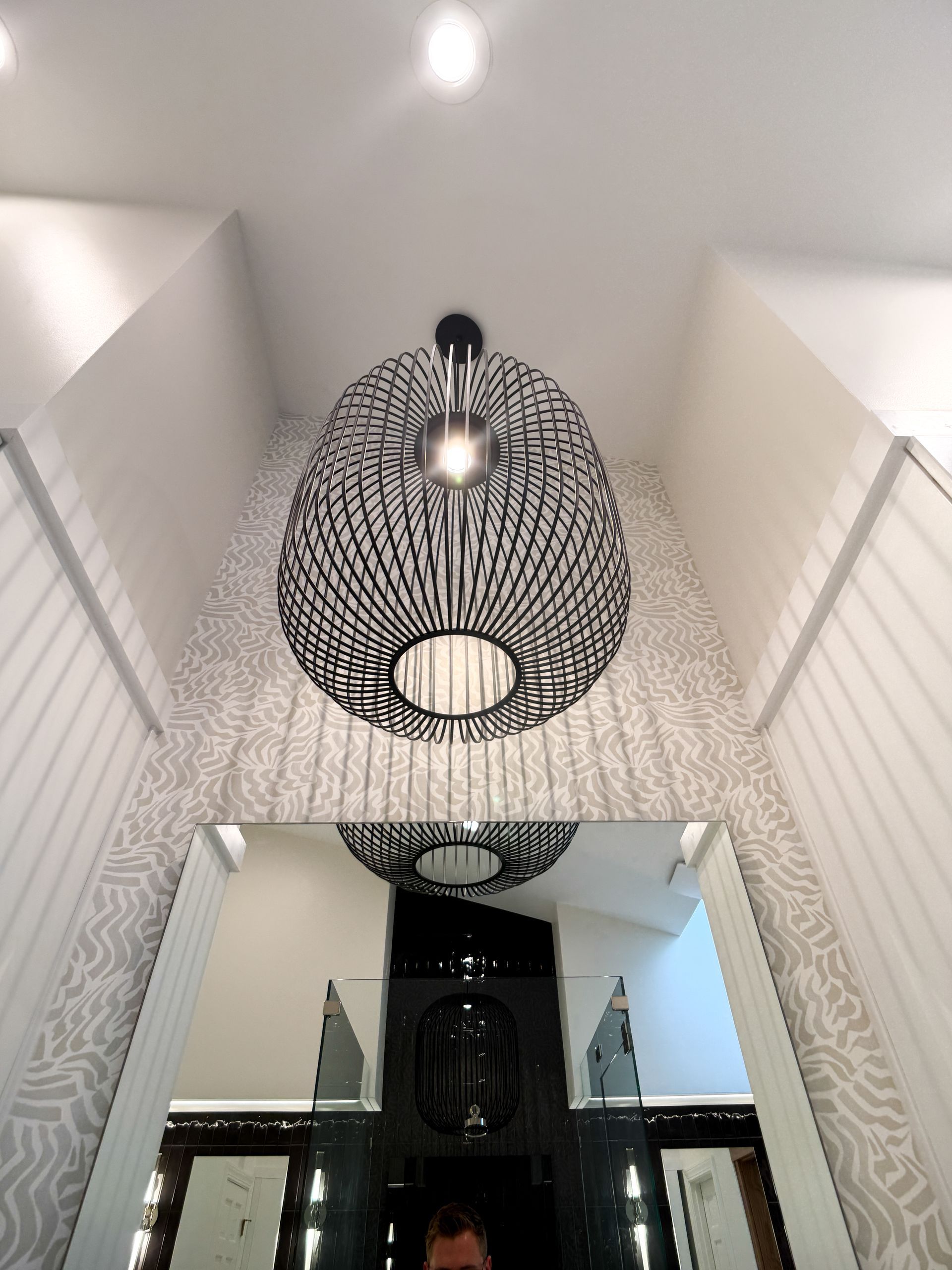 Ceiling view of a stairwell with black patterned pendant lights and white walls
