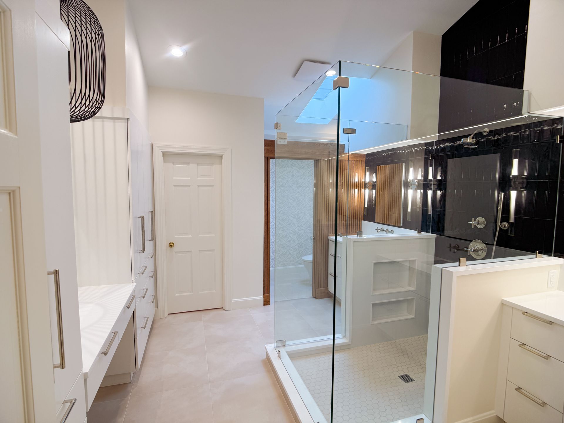 Modern bathroom with glass shower, white vanity, and beige tile in a bright hallway