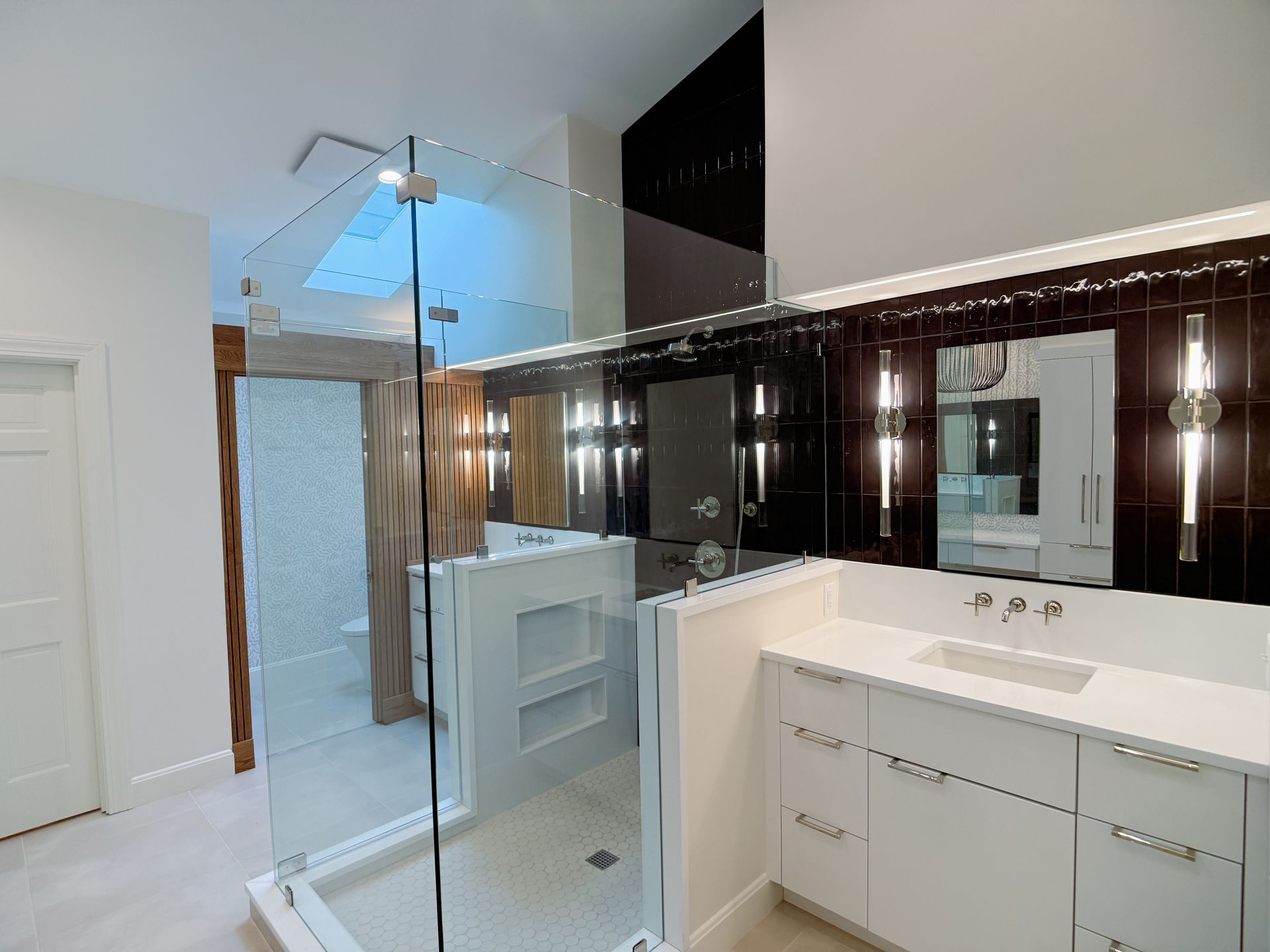 Modern bathroom with glass shower, white vanity, and dark mirrored cabinets